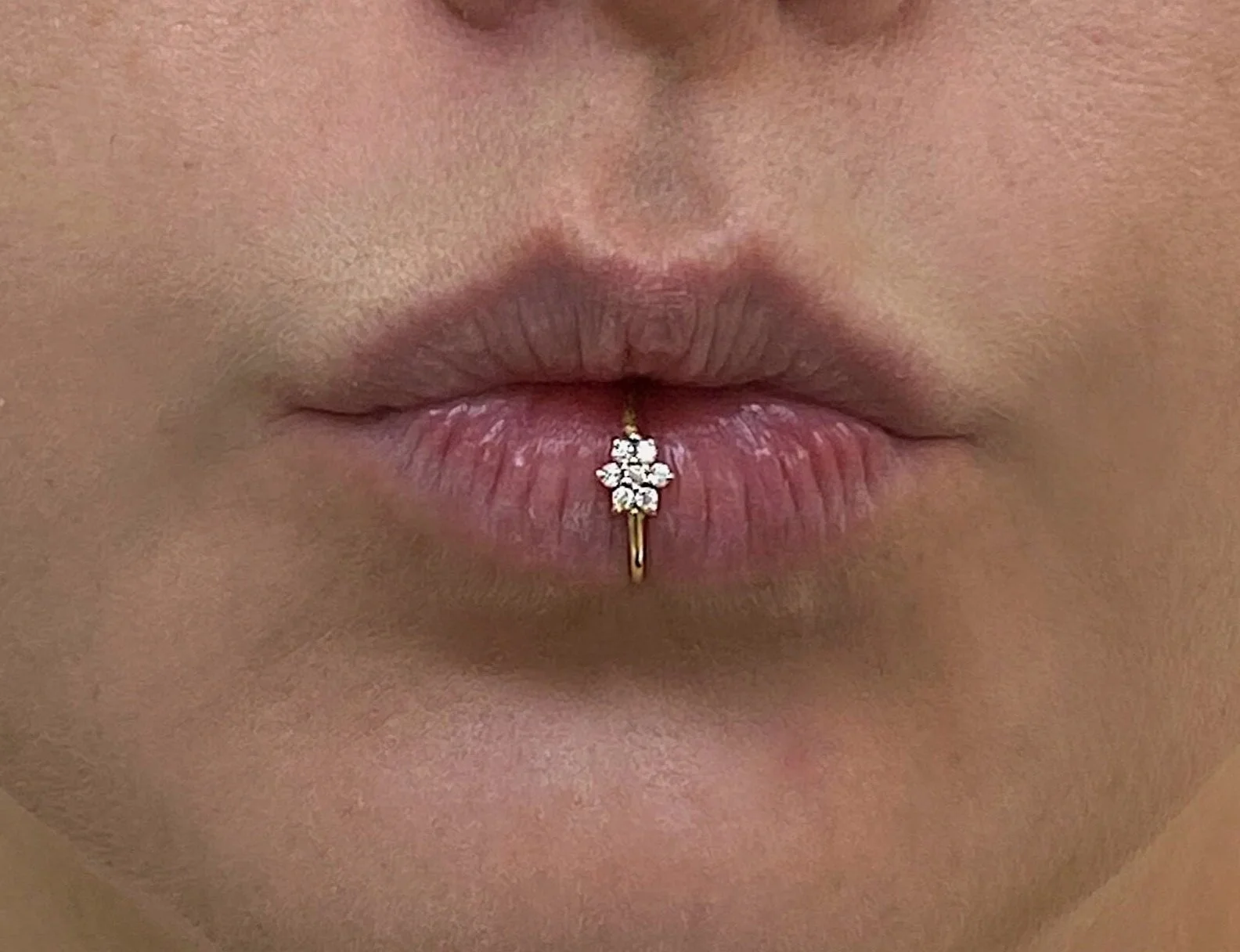 Close-up of a person's lips with a gold lip ring featuring a flower-shaped diamond design.