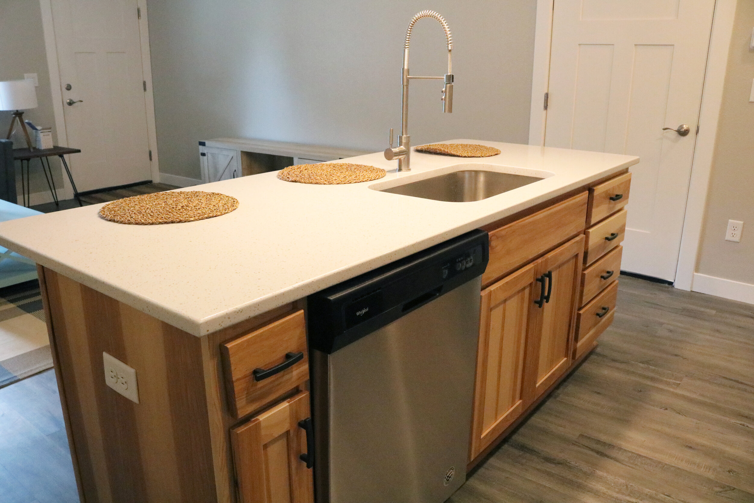 Modern kitchen island with cream countertop, built-in dishwasher, sink with pull-down faucet, wooden cabinets, and placemats on top.