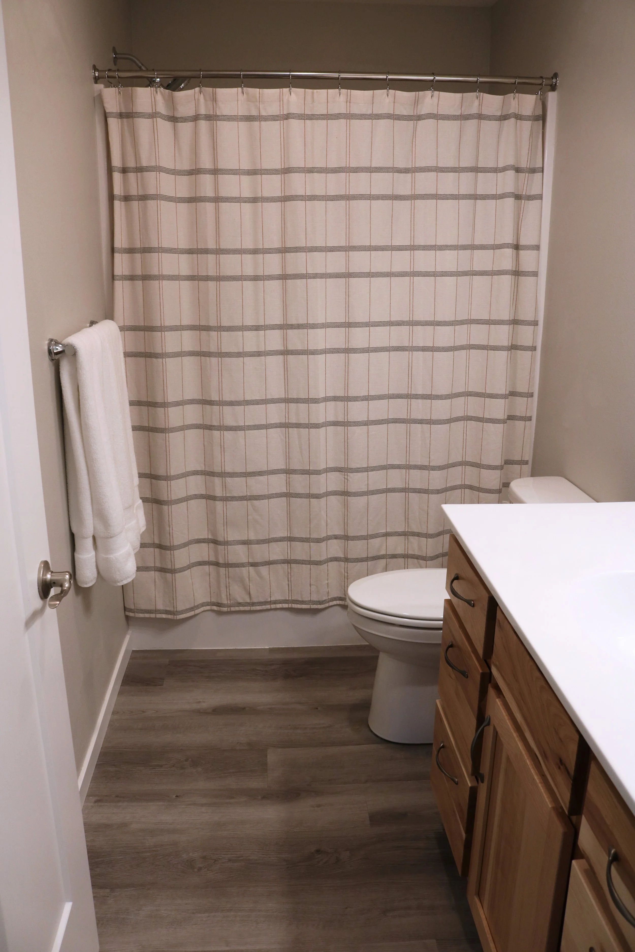 Bathroom with a plaid shower curtain, white toilet, wooden vanity with white countertop, and two white towels on a bar.