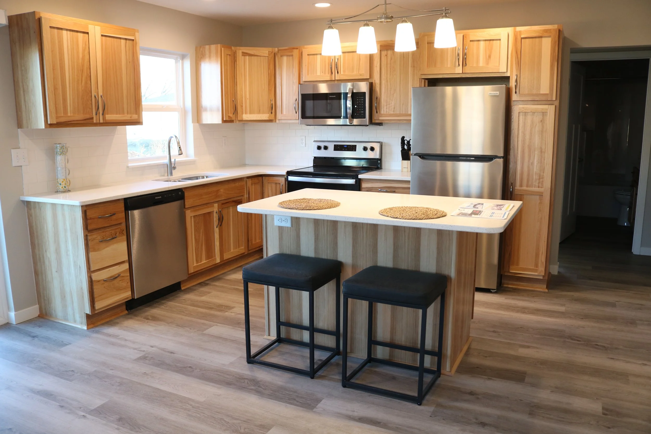 Modern kitchen with wooden cabinets, stainless steel appliances, and center island with seating. Features a refrigerator, oven, microwave, dishwasher, and wooden flooring.