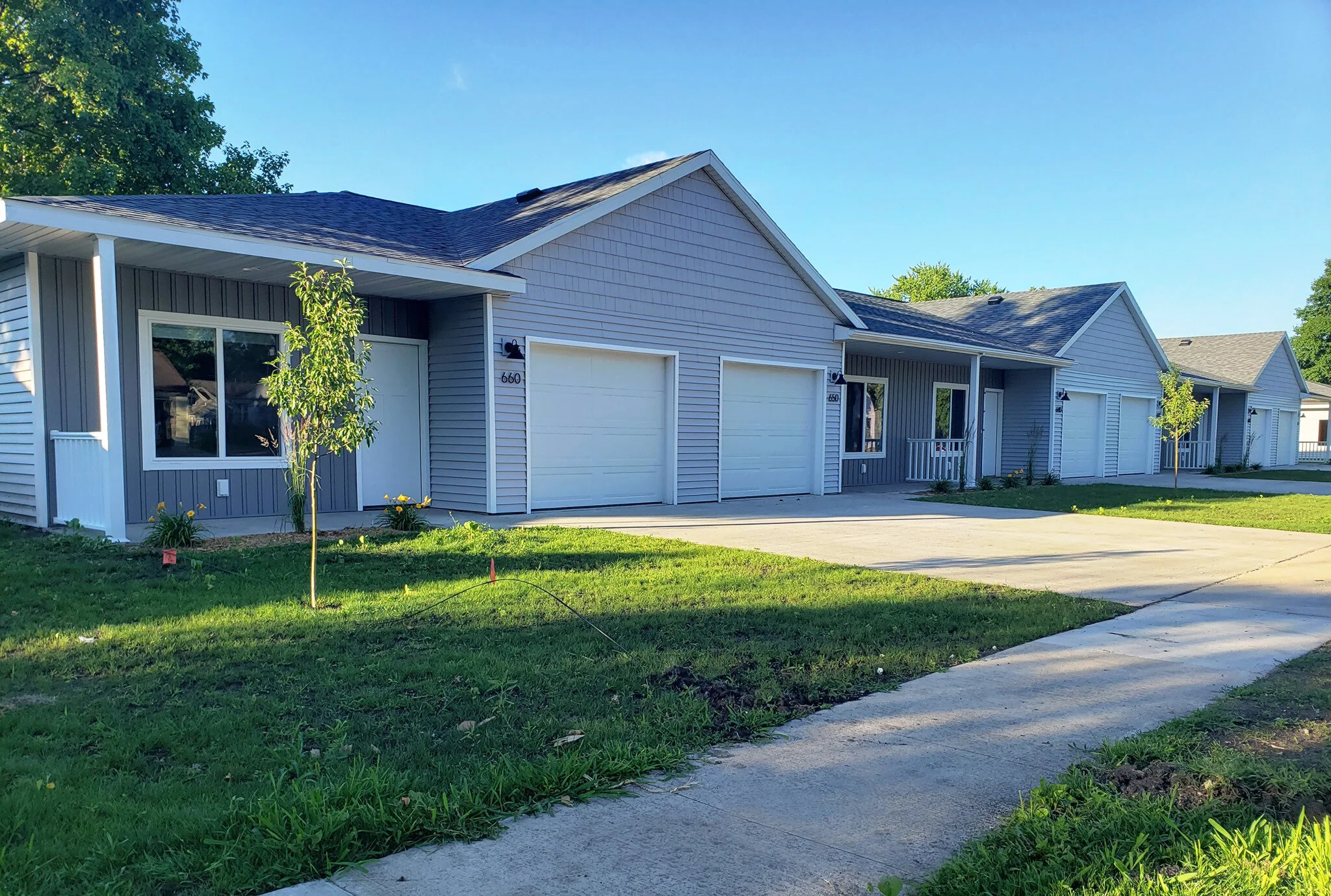 A row of modern, single-story suburban houses with attached garages, light gray siding, and small front lawns.