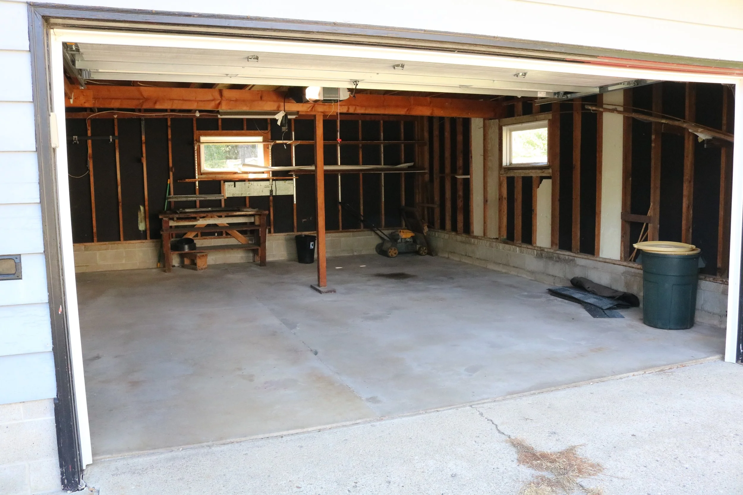 Empty garage with open door, concrete floor, workbench, window, and lawn mower