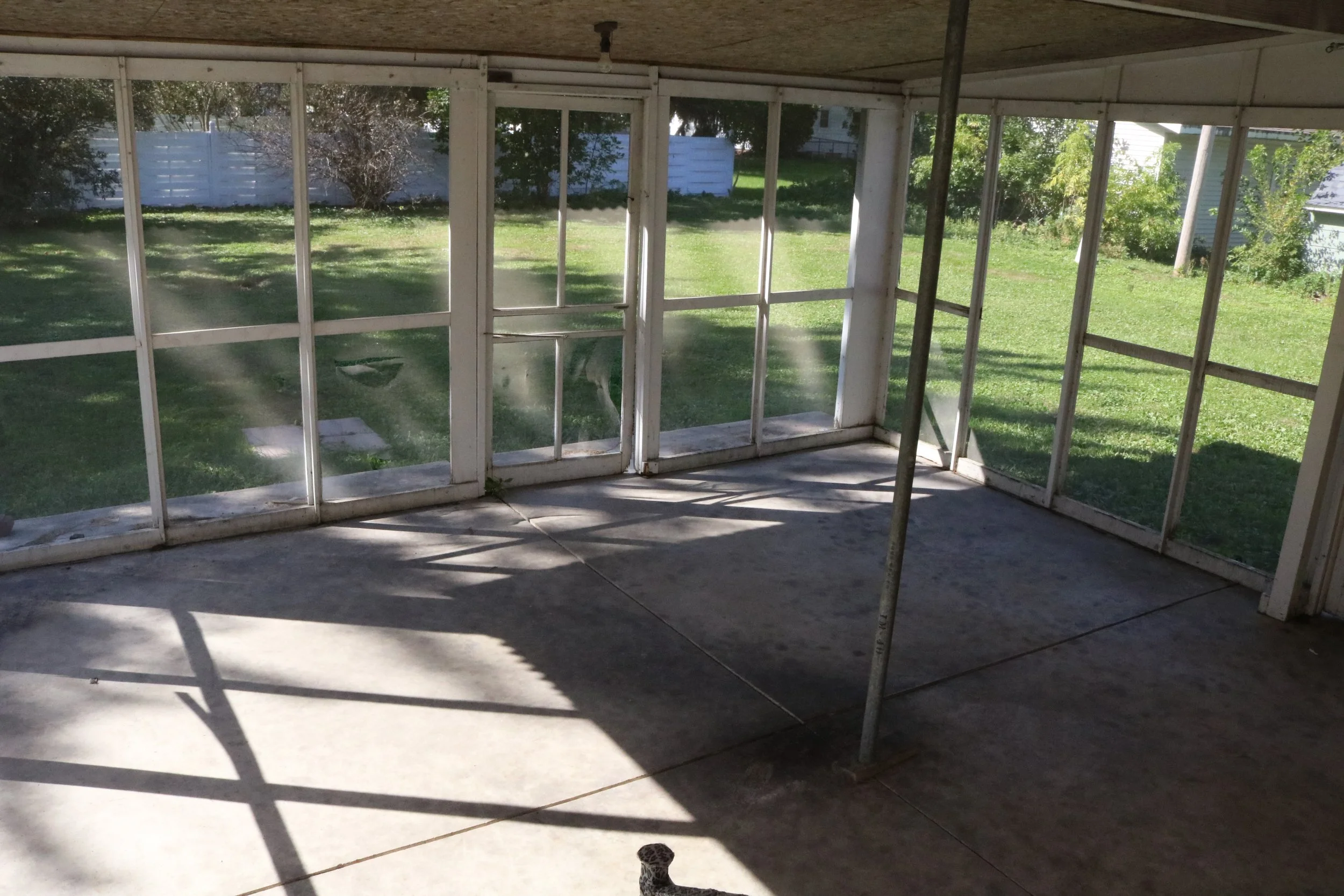 Empty screened porch with concrete floor and views of a grassy backyard.