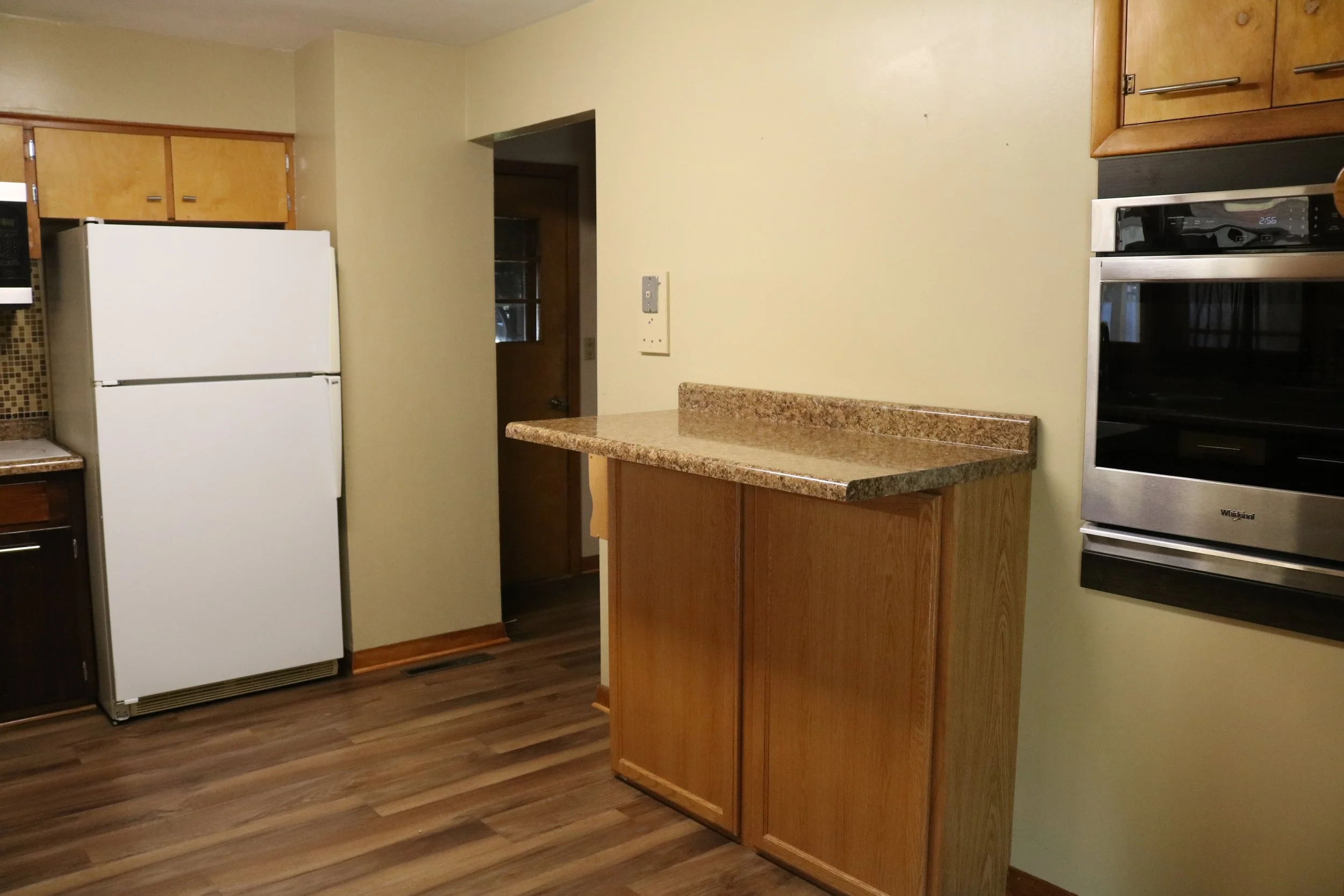 Kitchen with white refrigerator, built-in oven, wooden cabinets, and laminate flooring.