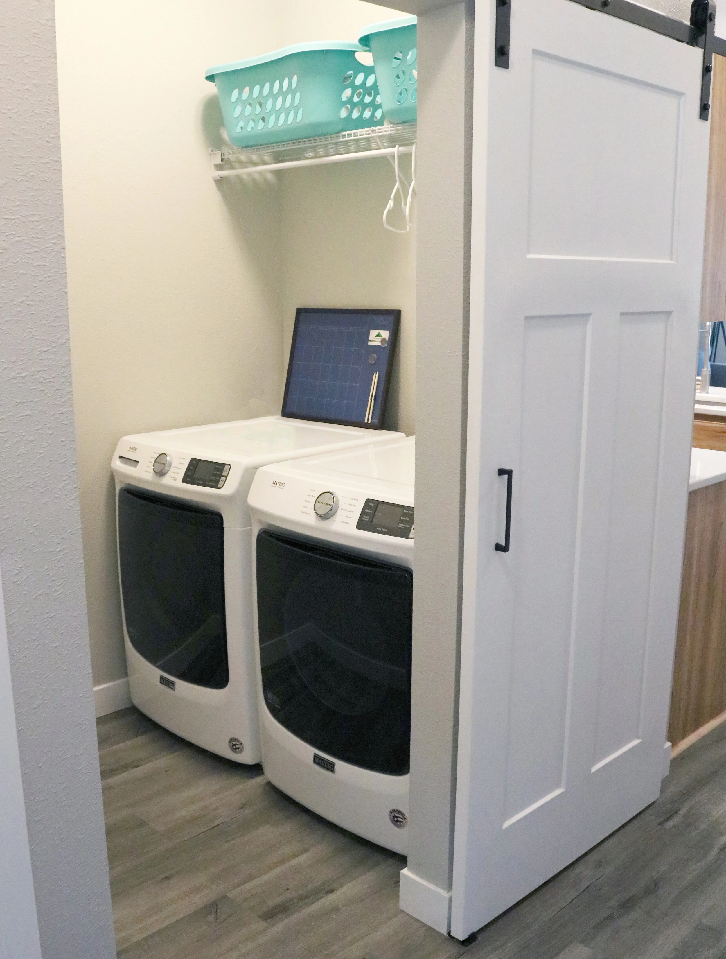Laundry room with washer and dryer, teal laundry basket on shelf, sliding door
