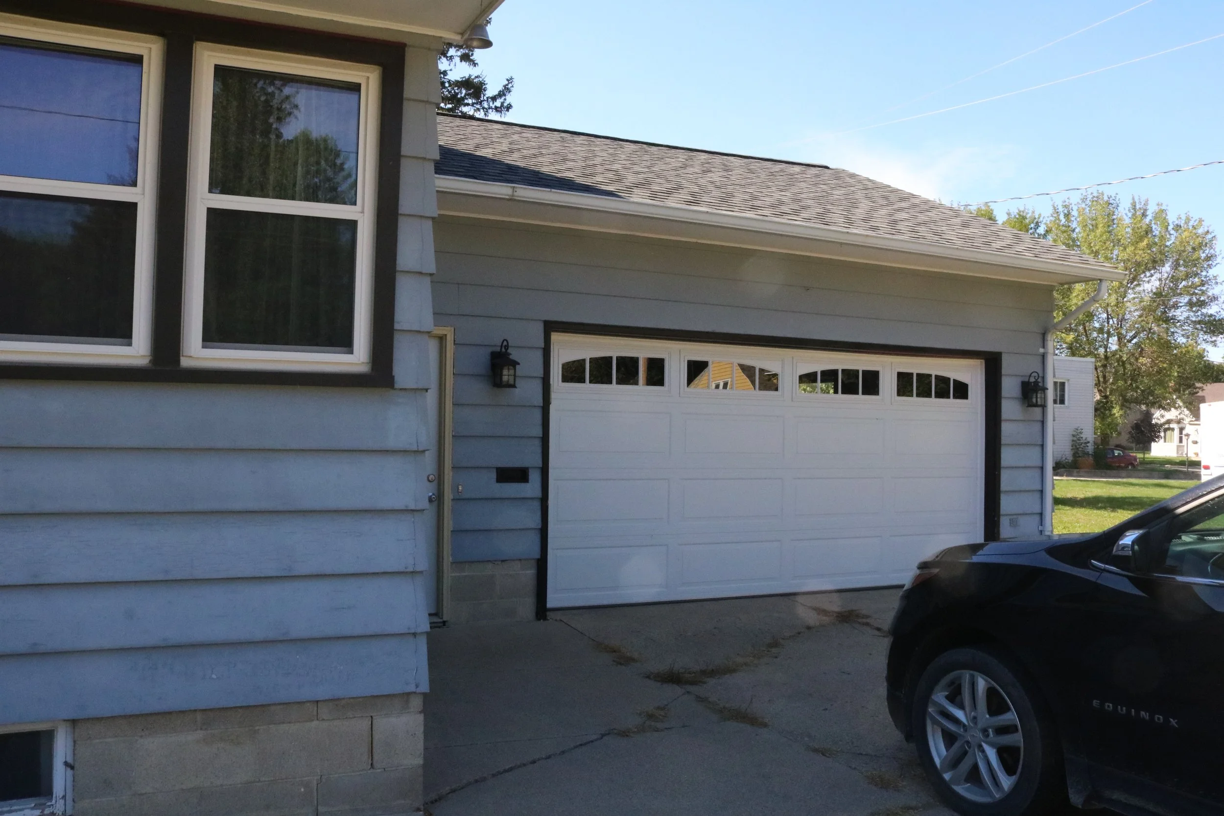 Suburban house with blue siding and a white garage door. A black car is parked in the driveway.