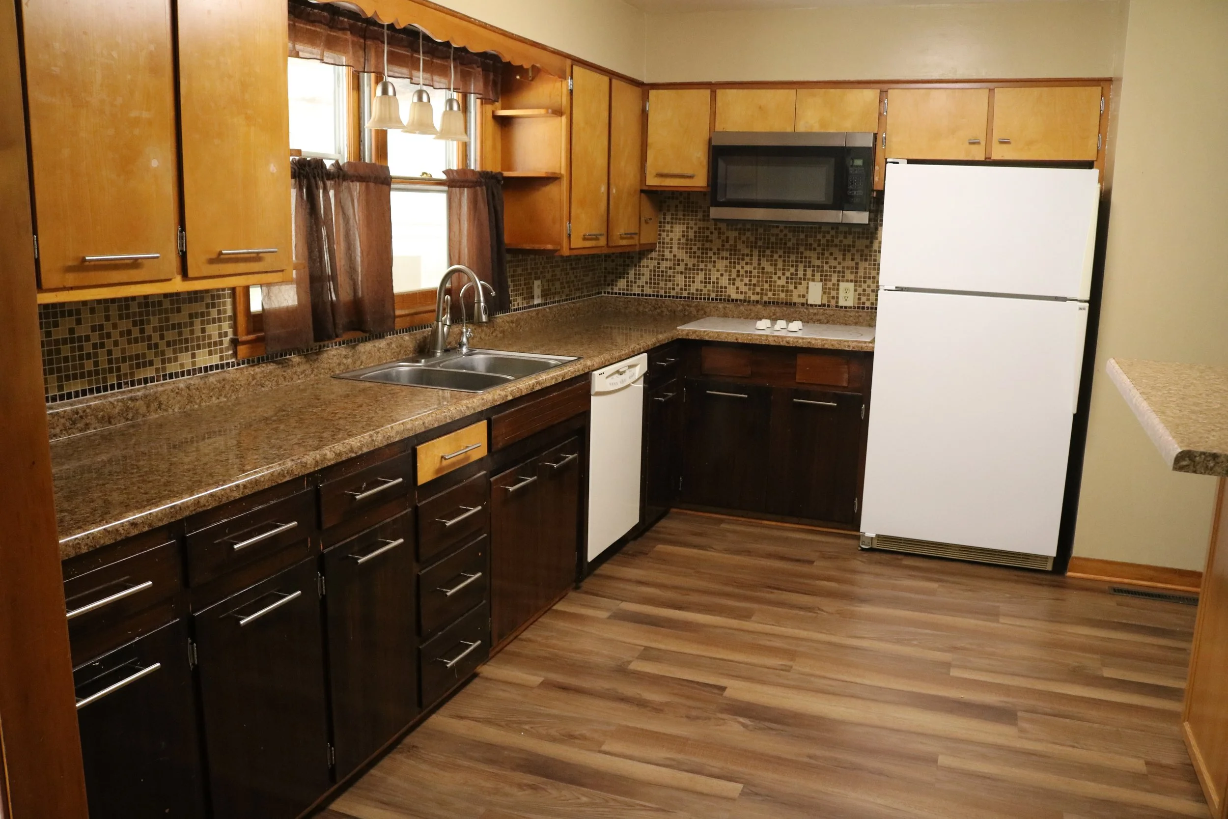 Modern kitchen with wooden cabinets, granite countertops, backsplash tile, stainless steel sink, white refrigerator, and microwave.