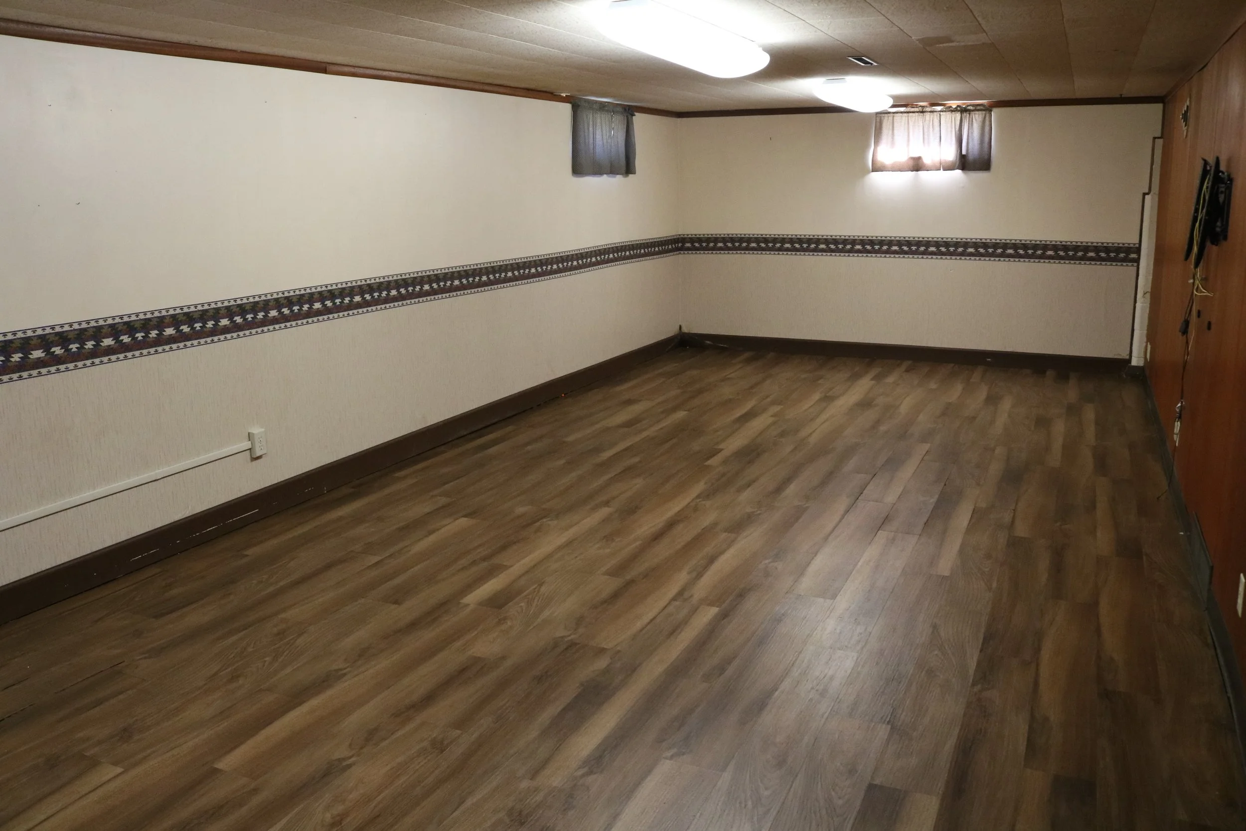 Empty room with wood flooring, patterned wallpaper border, and small windows.
