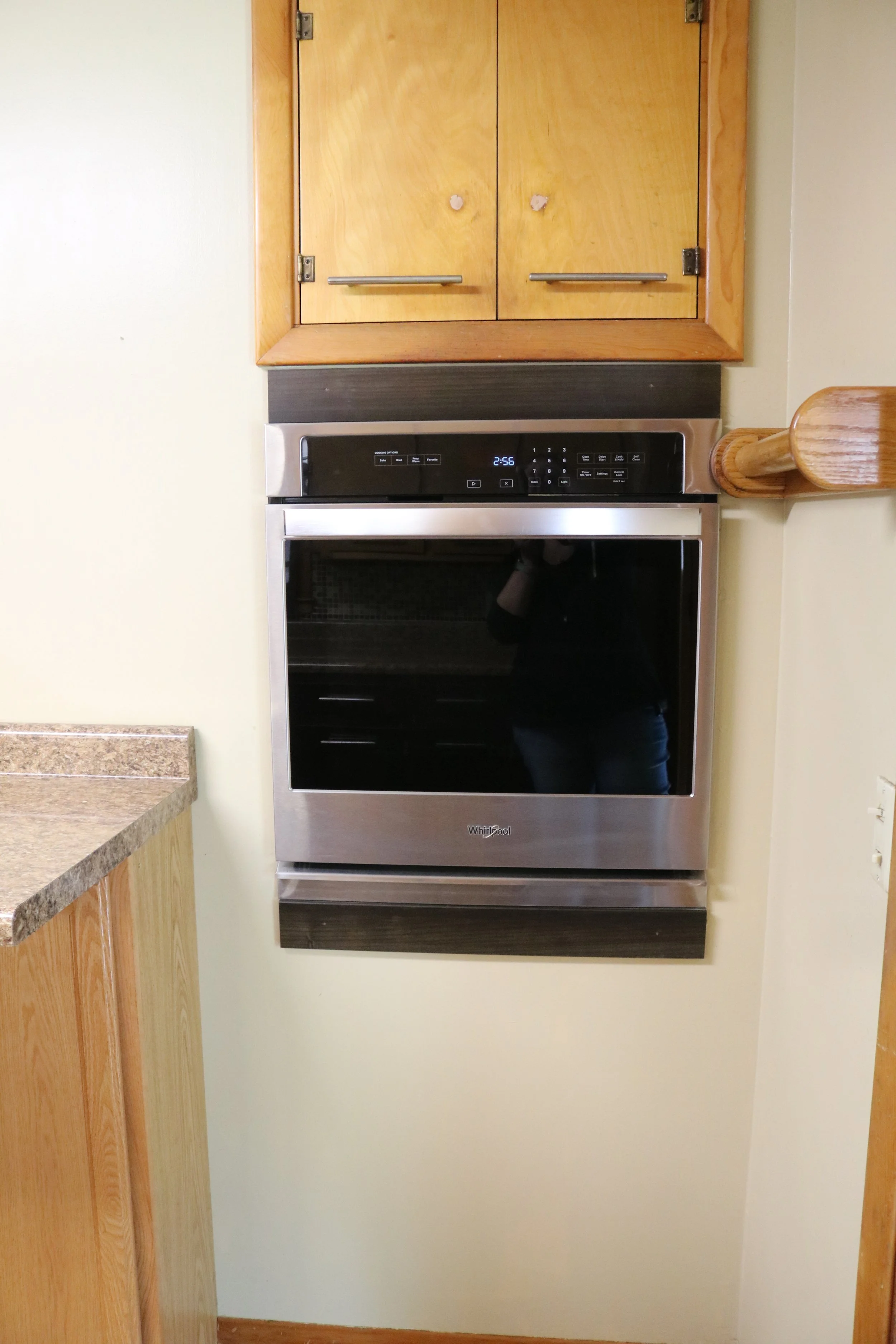 Wall-mounted stainless steel oven below wooden kitchen cabinets.