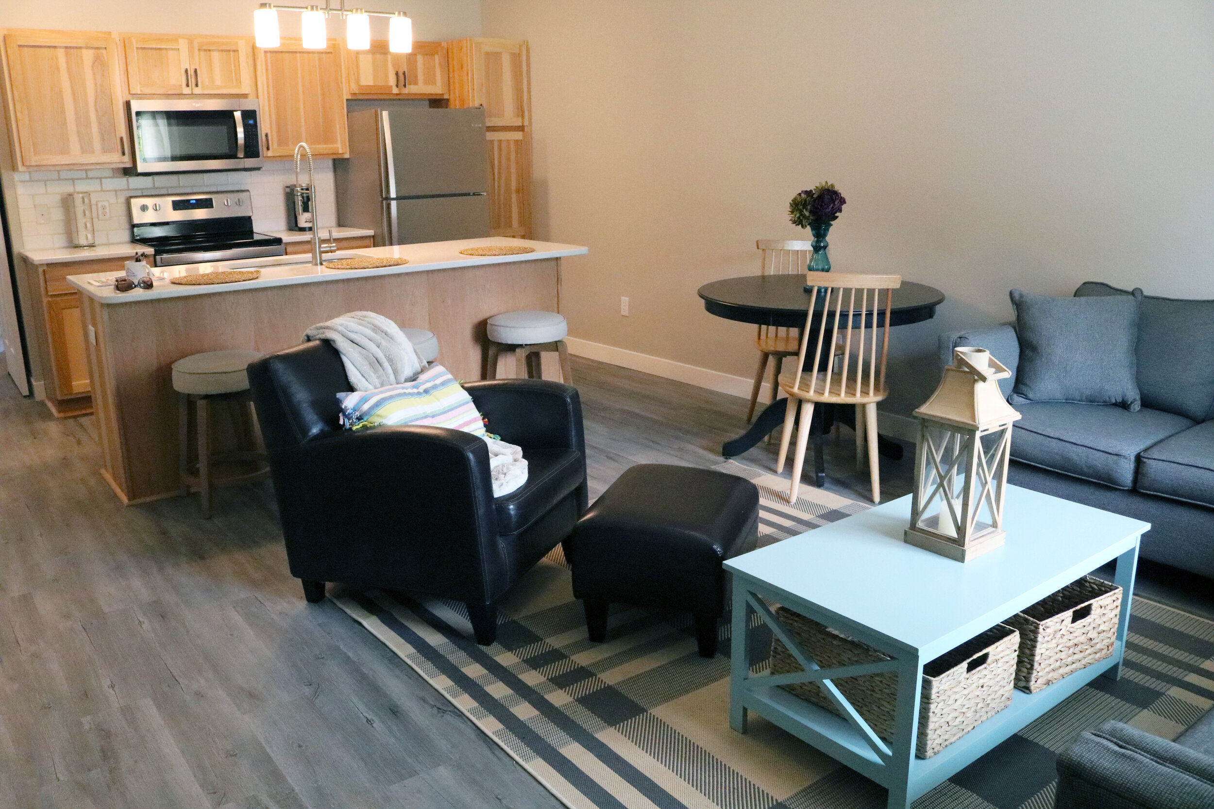 Modern living room and kitchen with wooden cabinets, a black round dining table, and a teal coffee table with basket storage.