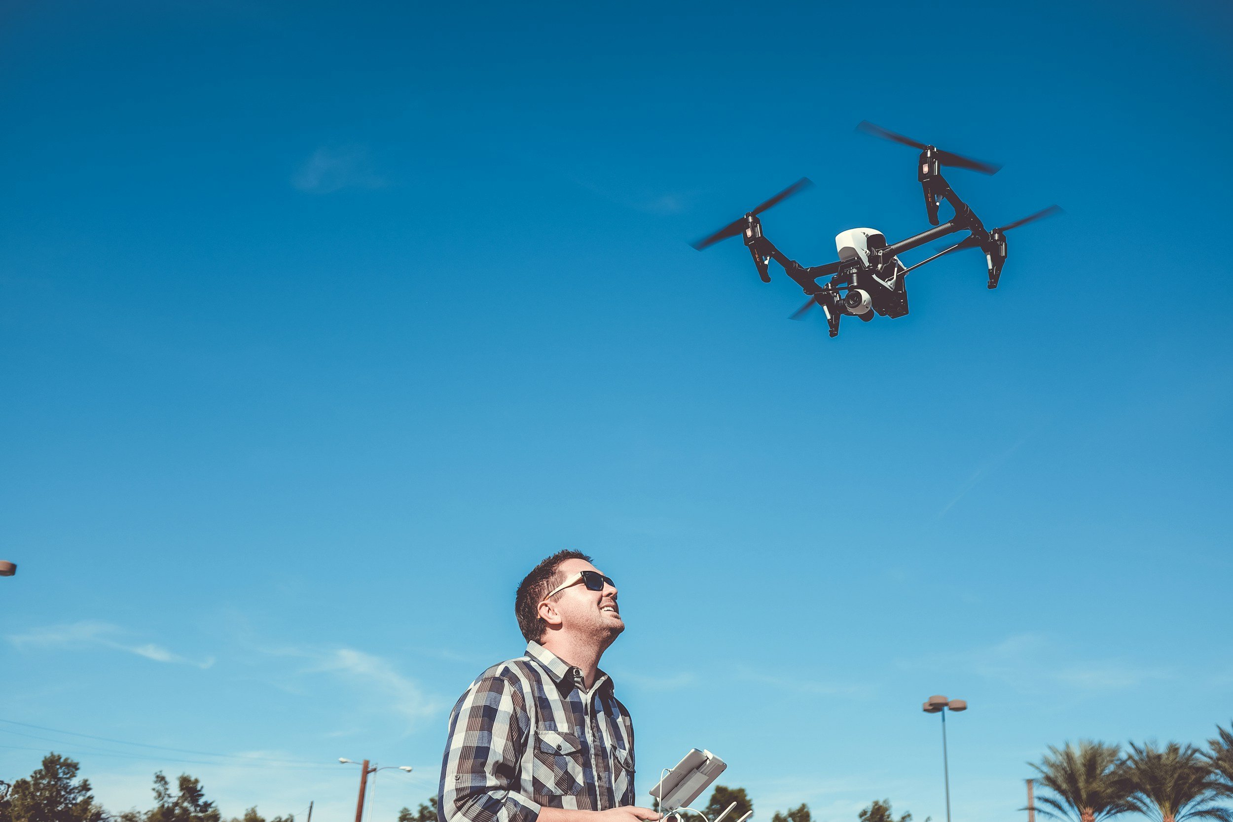 Man in plaid shirt and sunglasses operating a drone outdoors on a sunny day.