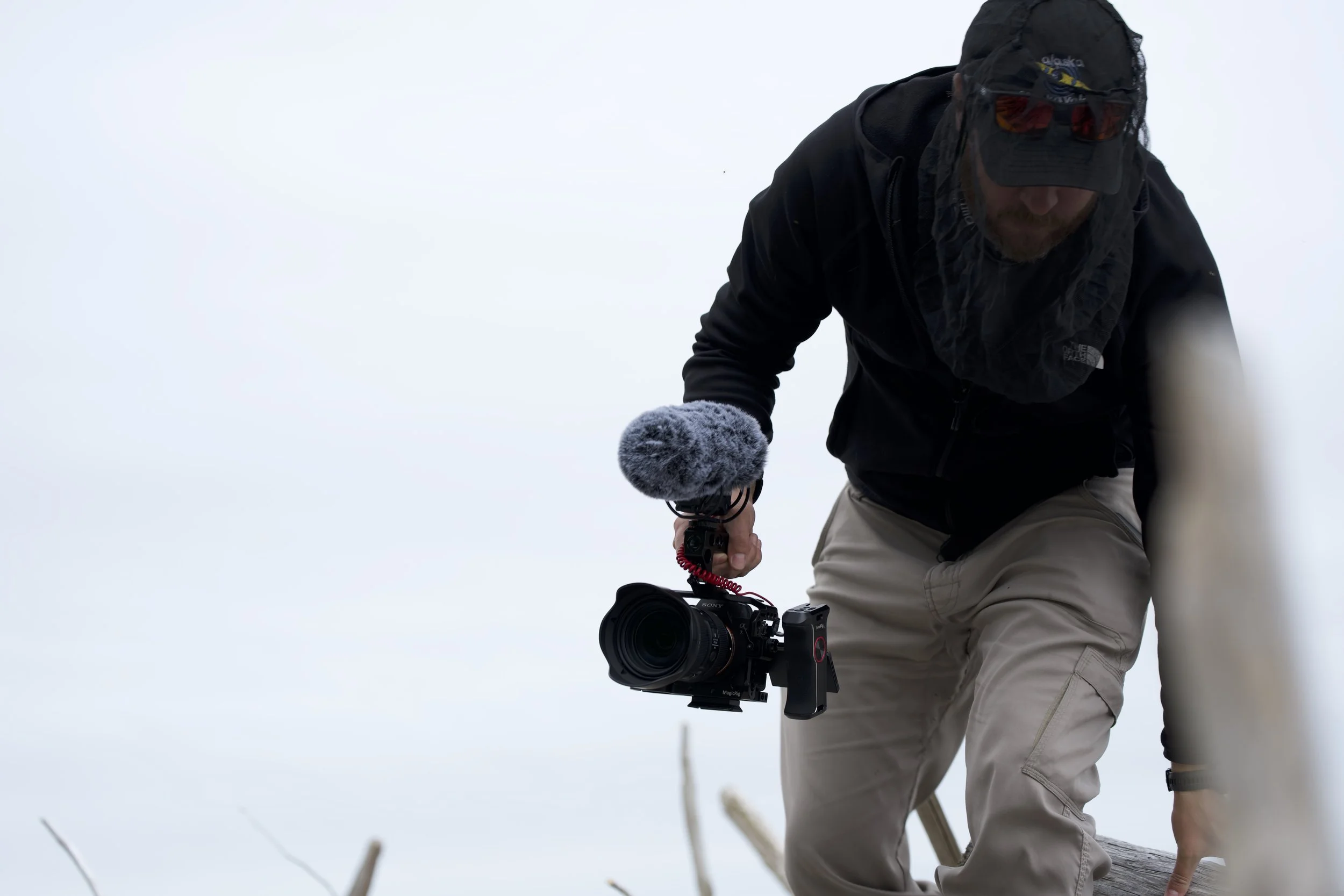 A man holding a camera with a microphone mounted on it, outdoors in a foggy or snowy environment.