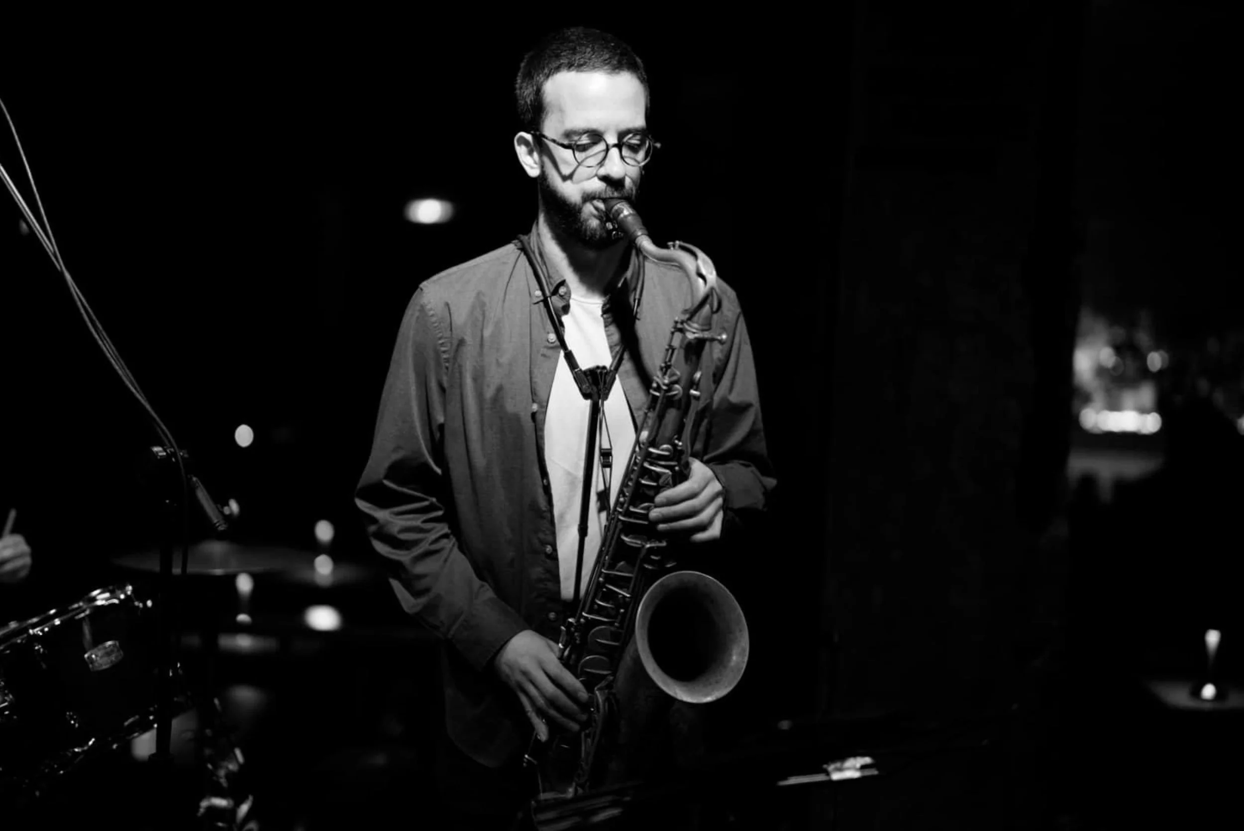 A man playing a saxophone during a performance in a dimly lit setting, in black and white.