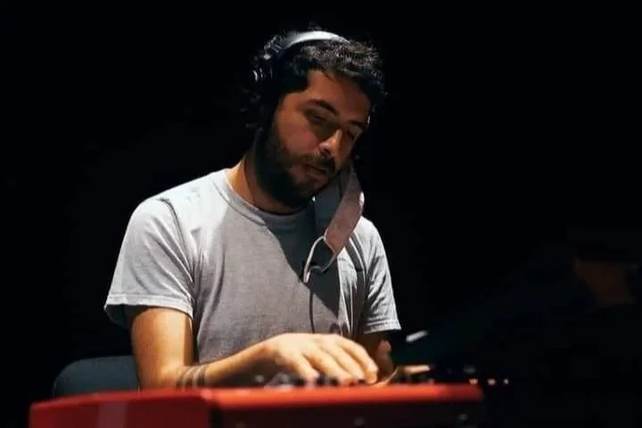A man with headphones is using a red keyboard or synthesizer in a dark environment.