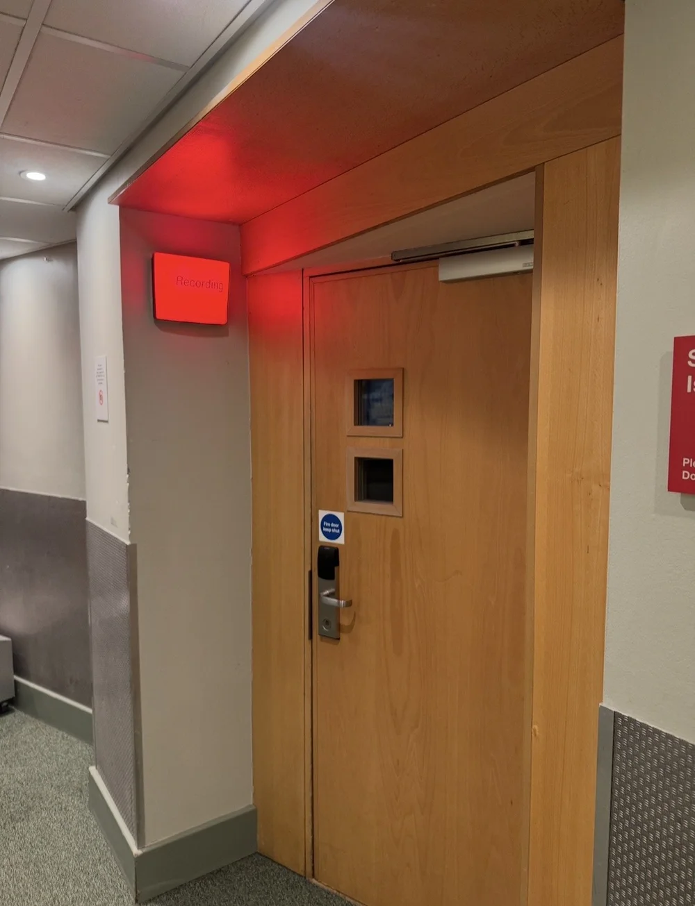 A closed studio door with a lit red Recording sign above it.
