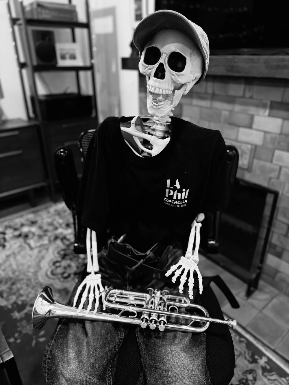 A skeleton in jeans, a ball cap, and an LA Phil T-shirt, slumped in a wooden chair holding a pocket trumpet.
