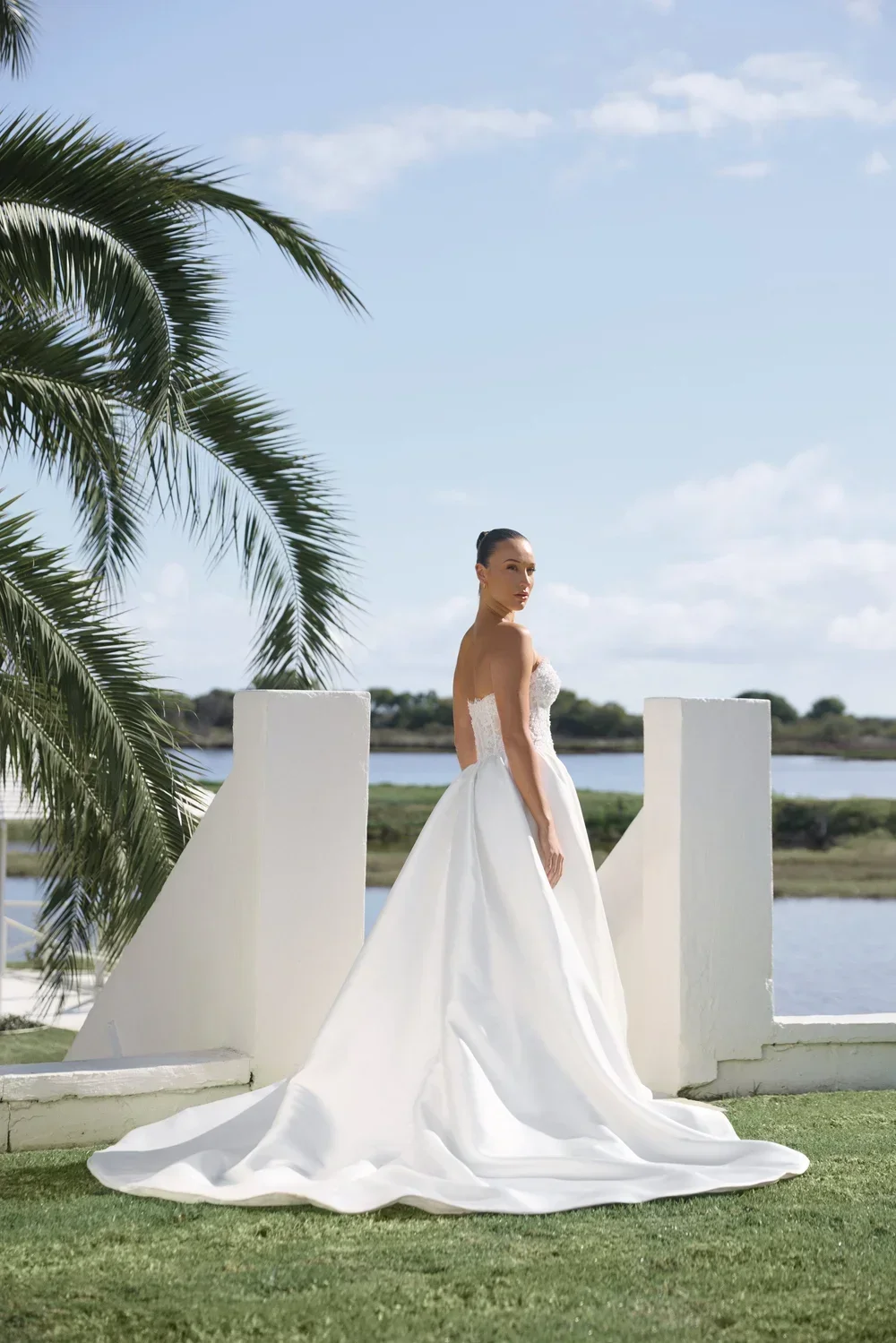 Bride wearing a Florence strapless white gown with long train by the water
