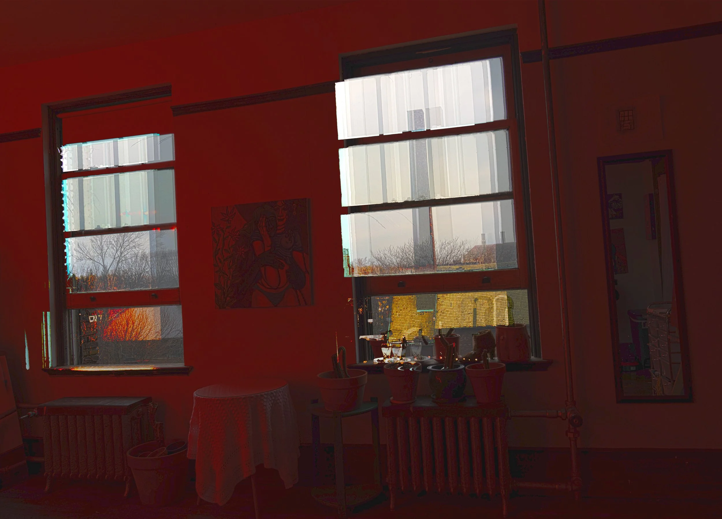 Room with large windows, red-painted walls, a small round table with a white tablecloth, potted plants, a framed artwork, and a mirror reflecting part of the room.