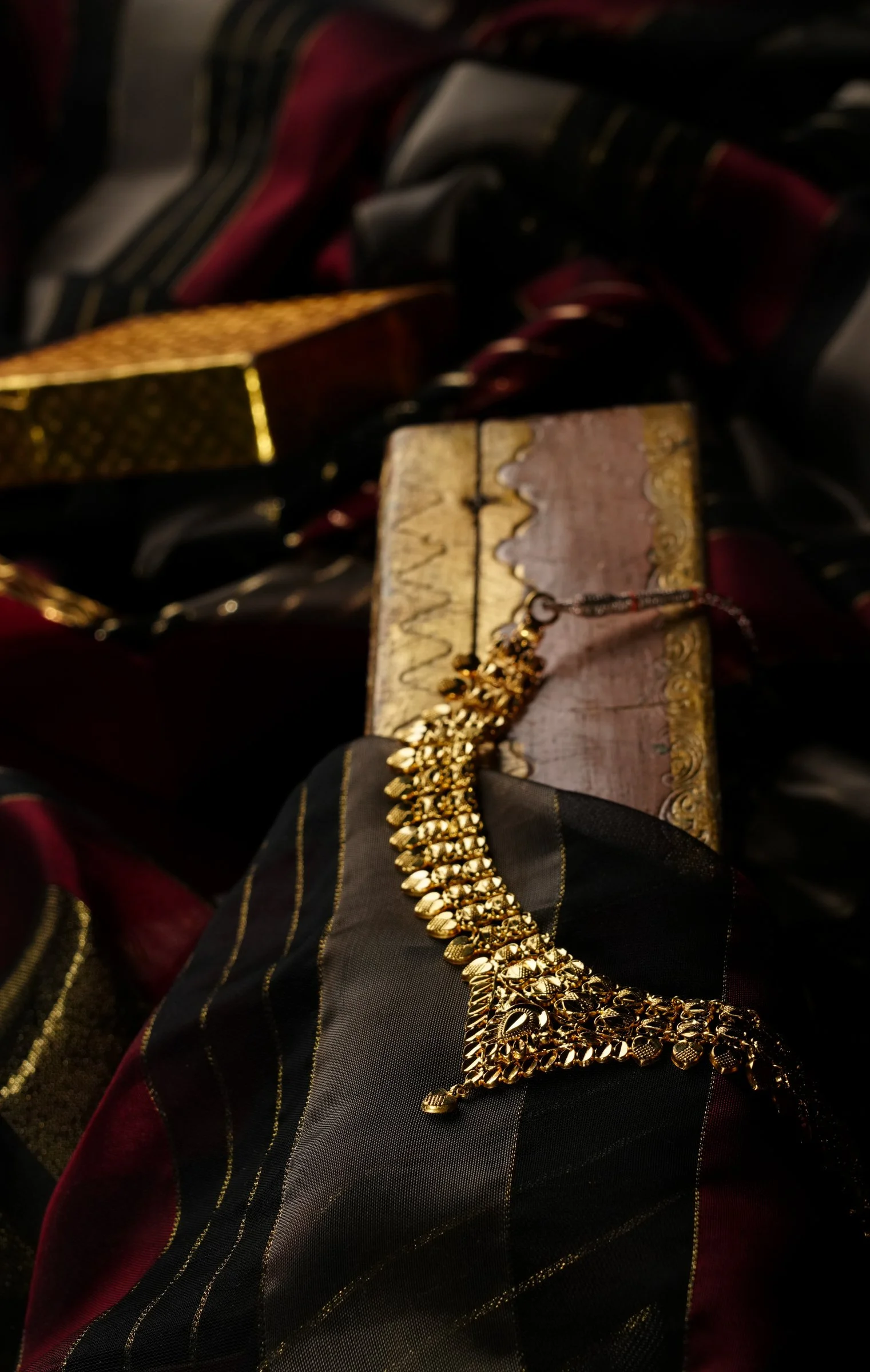 Gold necklace placed on a black and red striped fabric, with other jewelry and accessories in the background.