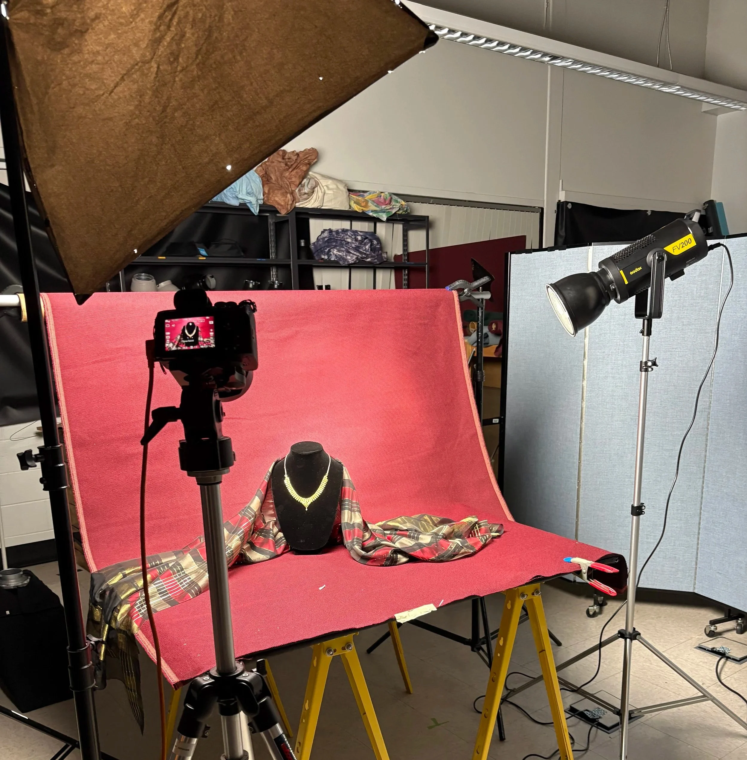 A jewelry photography setup with a necklace on a mannequin bust, a light tent, tripods, and studio lighting in a room with shelves and storage in the background.