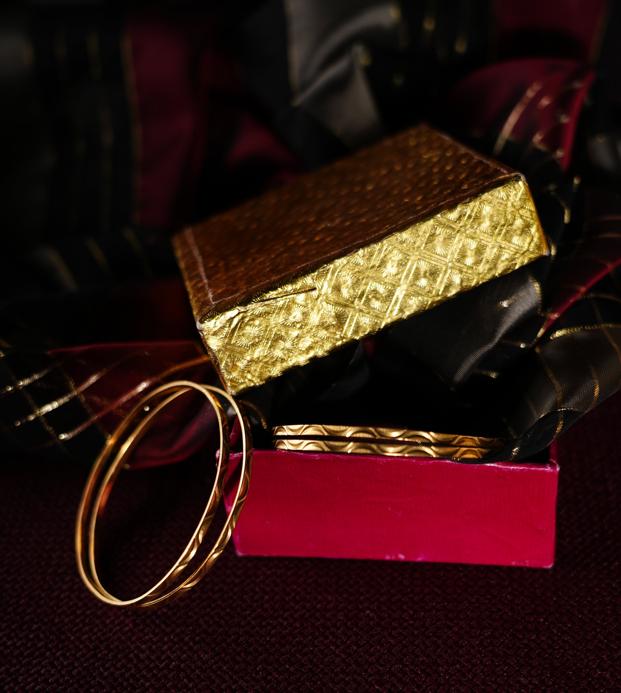 Gold and brown bracelets and a gold clutch purse on a pink box, with a dark background.