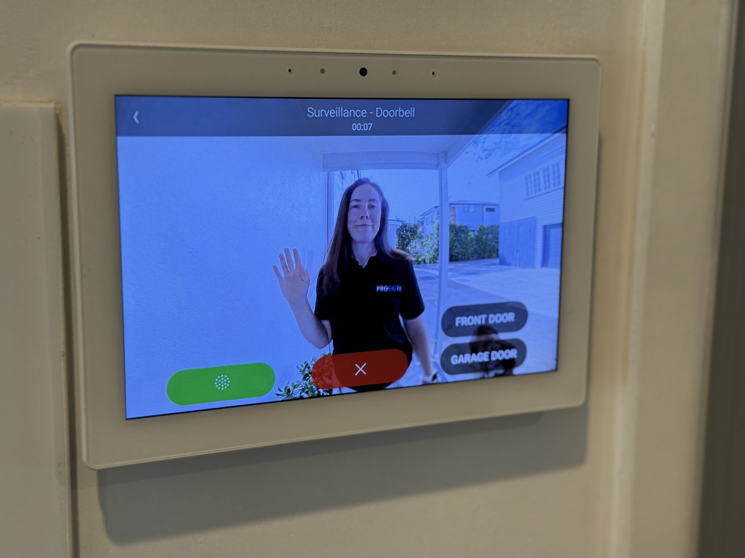 Digital doorbell display showing a woman waving outside, with buttons labeled 'Front Door' and 'Garage Door' on screen.