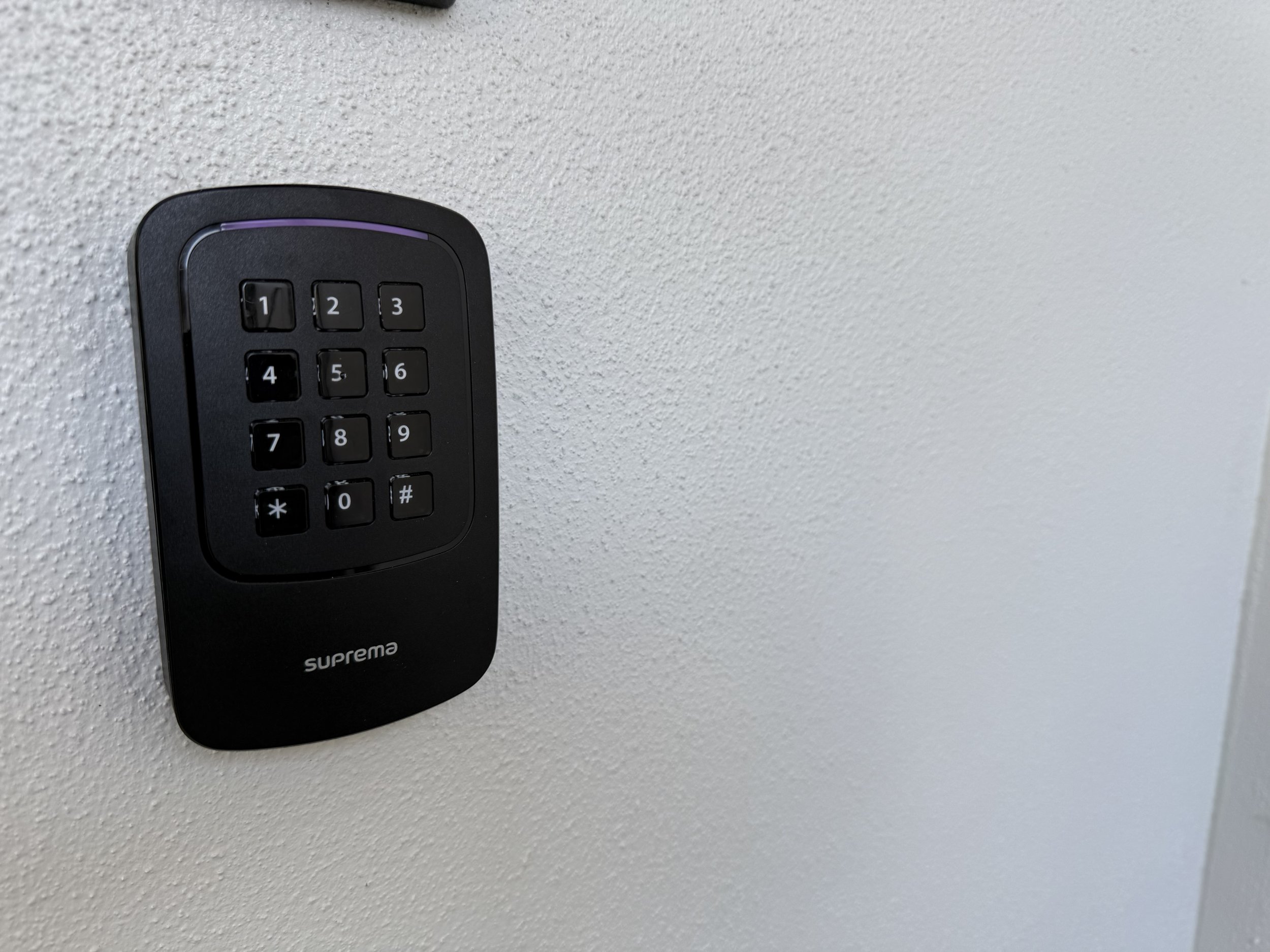 Black keypad access control system mounted on a white wall.