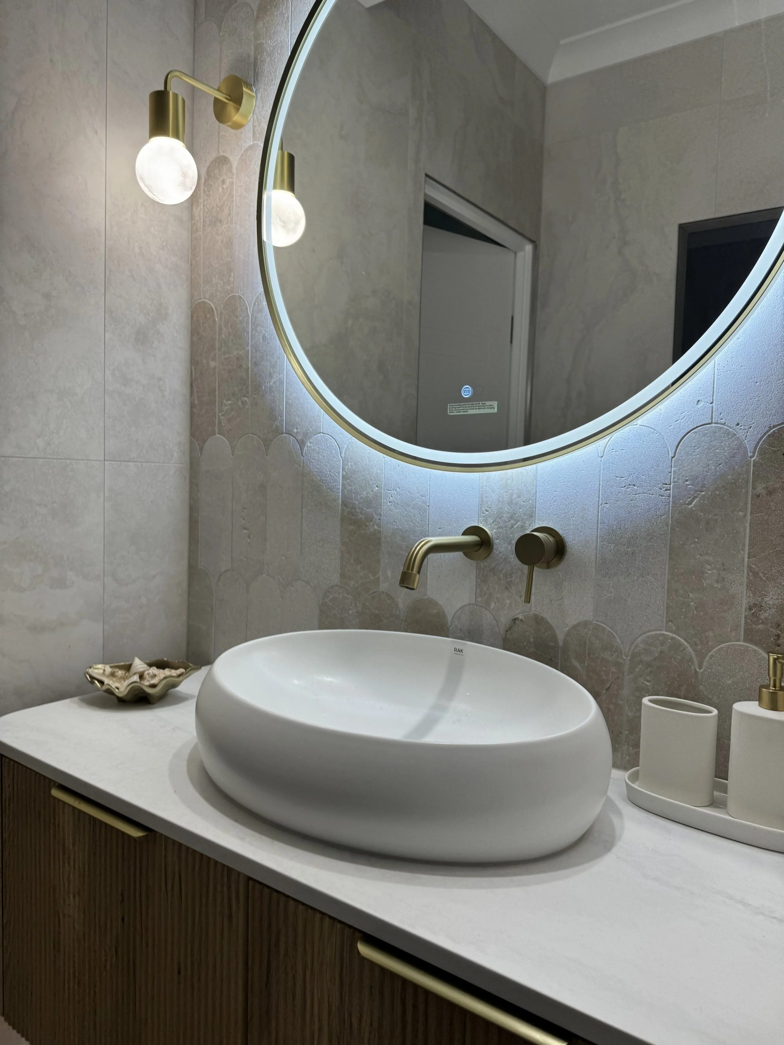 Modern bathroom sink with an oval mirror and stylish lighting fixtures.