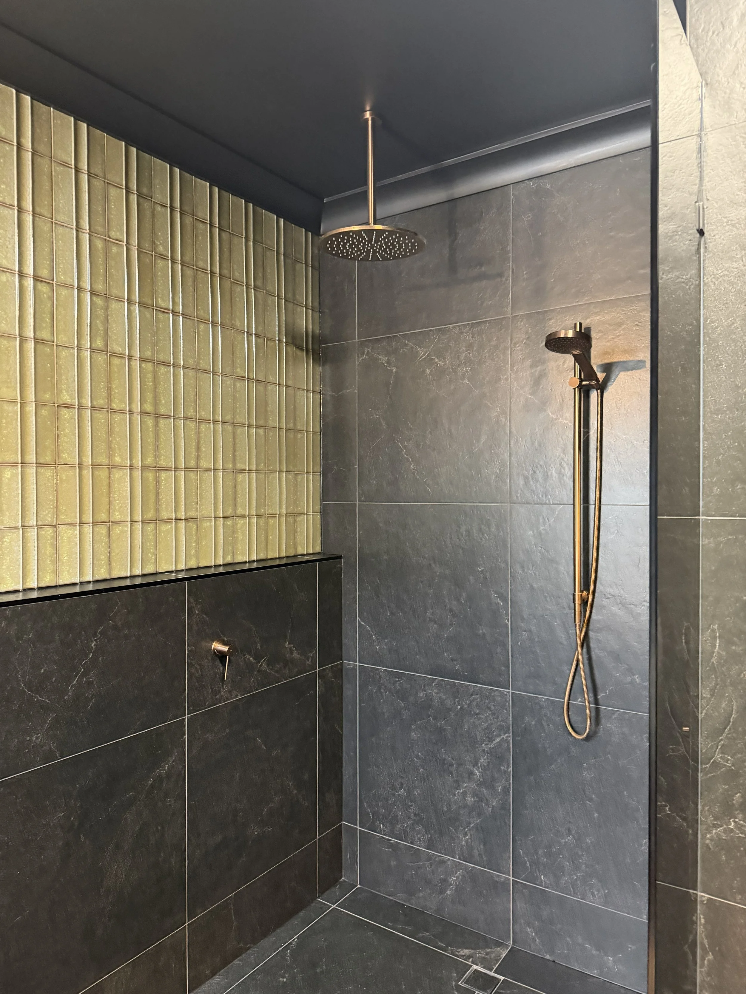 Modern shower with dark gray tiles, a green tiled accent wall, a rainfall showerhead, and a handheld showerhead.