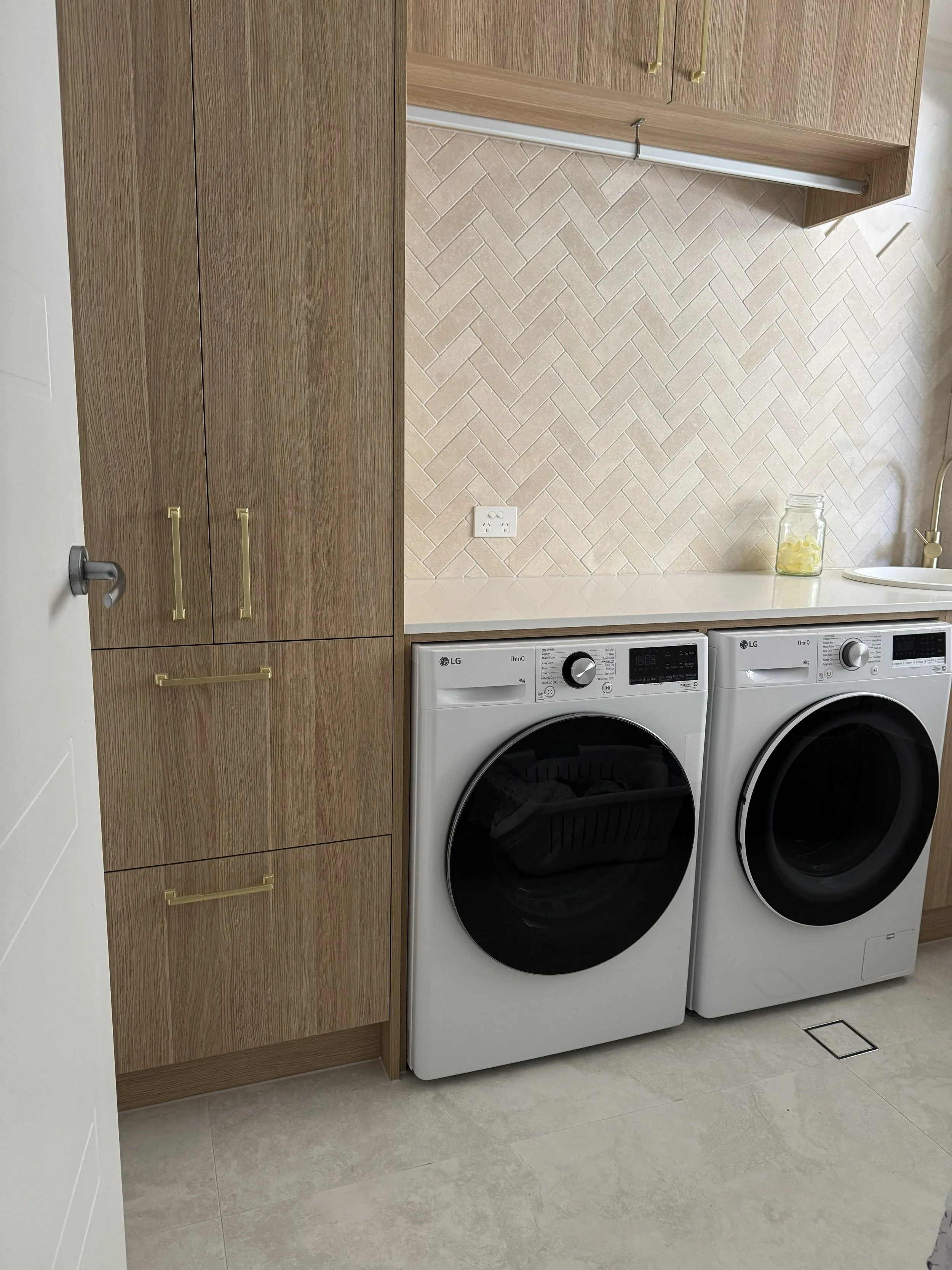 A laundry room with wooden cabinets, a backsplash with a herringbone tile pattern, and a white washing machine and dryer side by side.
