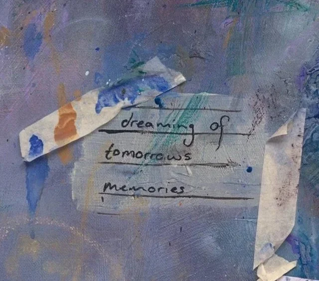 A close up detail photo of “Tomorrows’ Memories” artwork.  A piece of torn paper with handwritten words 'dreaming of tomorrow's memories' on a colorful, painted background.