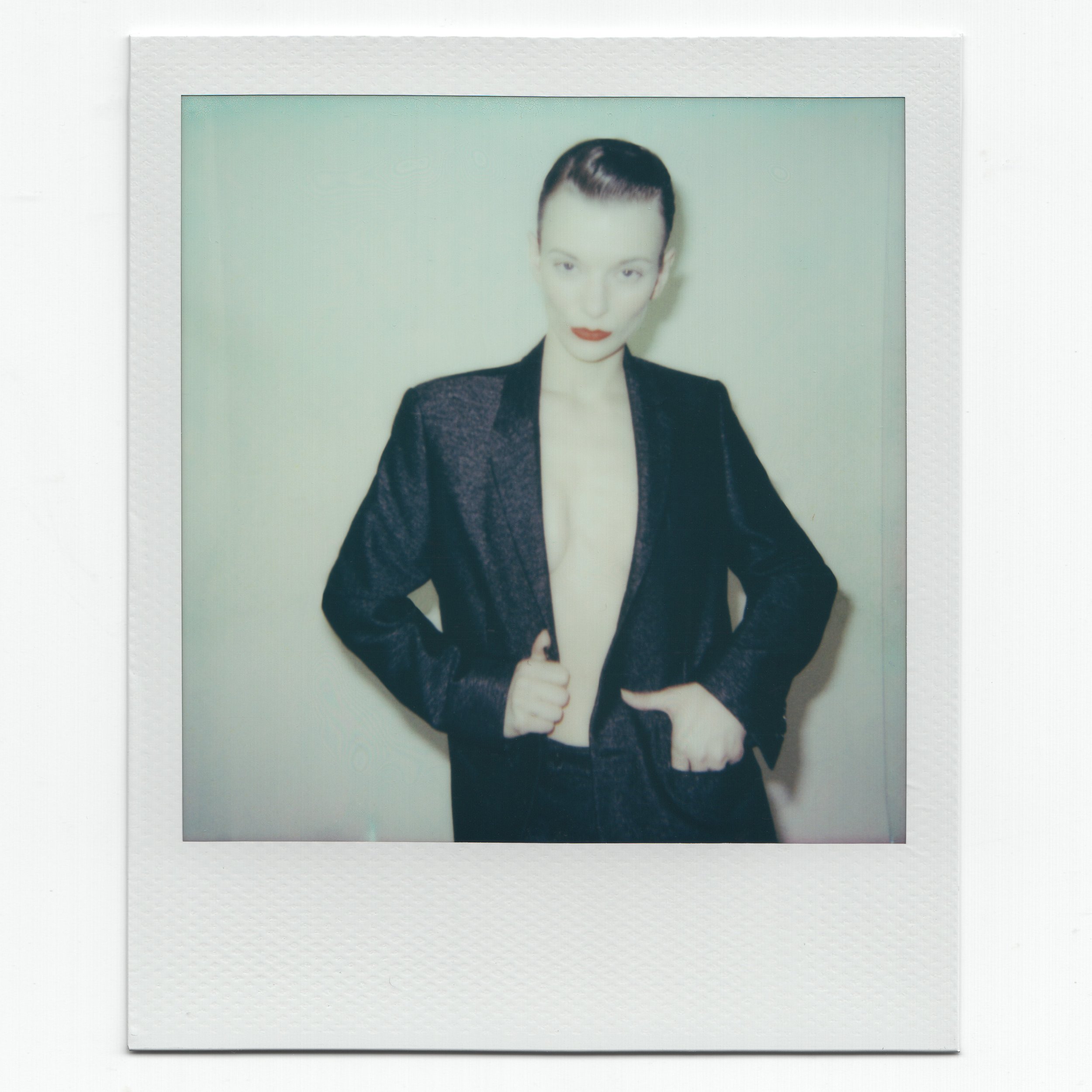 Model in a black Dior Homme by Hedi Slimane blazer without a shirt underneath, posed confidently, against a plain background.