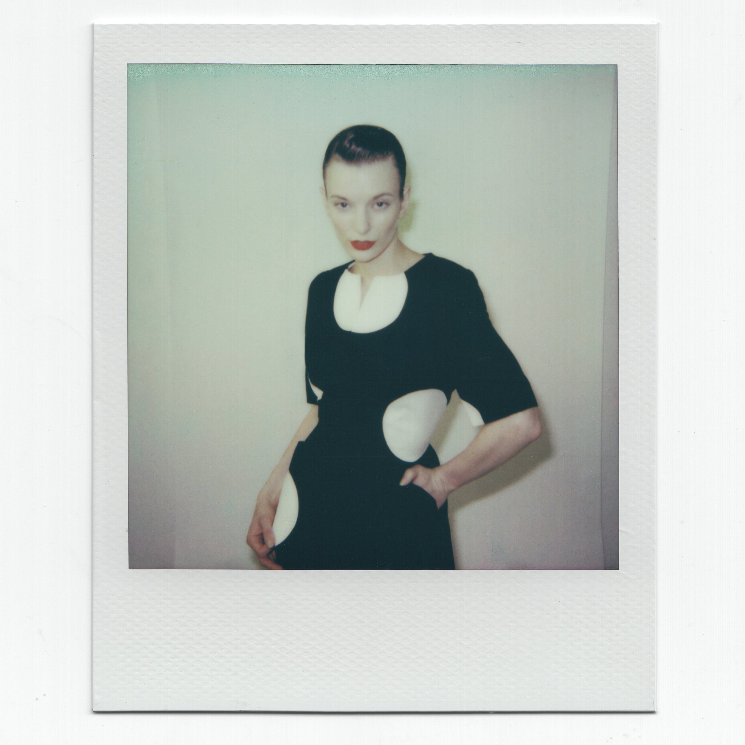 Model wearing a black Thierry Mugler suit with white circular patterns, posed against a plain background.