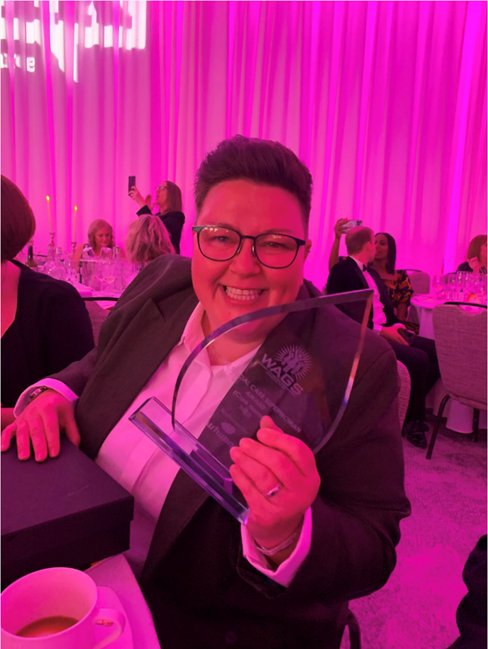 Woman smiling and holding an award at a formal event with pink lighting.
