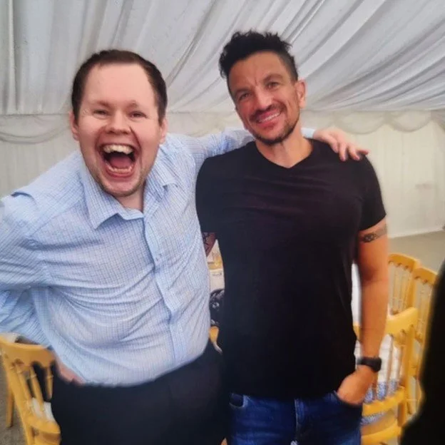 Two men smiling and posing for a photo inside a decorated event tent with yellow chairs in the background.