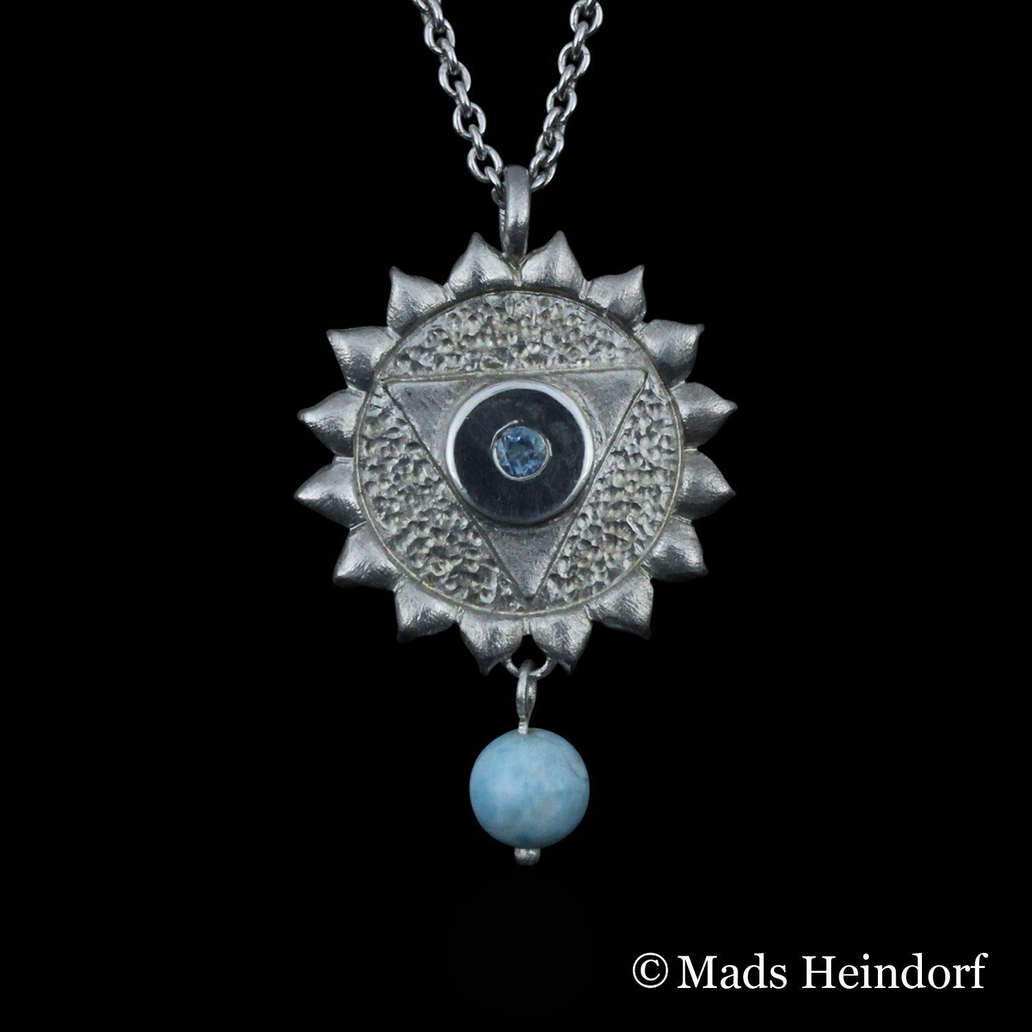 Halschakra er et håndlavet halssmykke af sterling sølv med 3 facetslebne blå akvamariner og 1 blå stenperle af larimar fra kollektionen Chakra af Guldsmed Heindorf.
