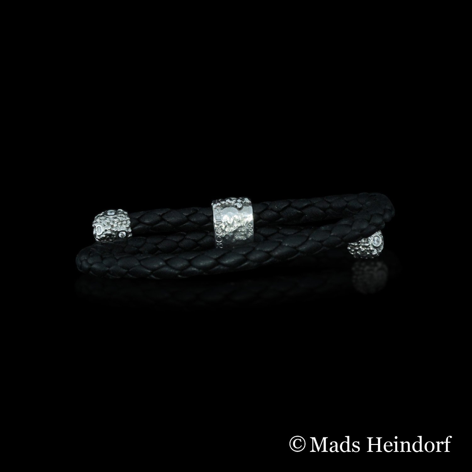 Håndlavet armbånd af 18K rødguld med 3 facetslebne ubehandlet blålig spinel, 14 brillantslebne diamanter på I alt 0,15 carat og sort flettet lædersnor fra kollektionen Myriader af Guldsmed Heindorf.