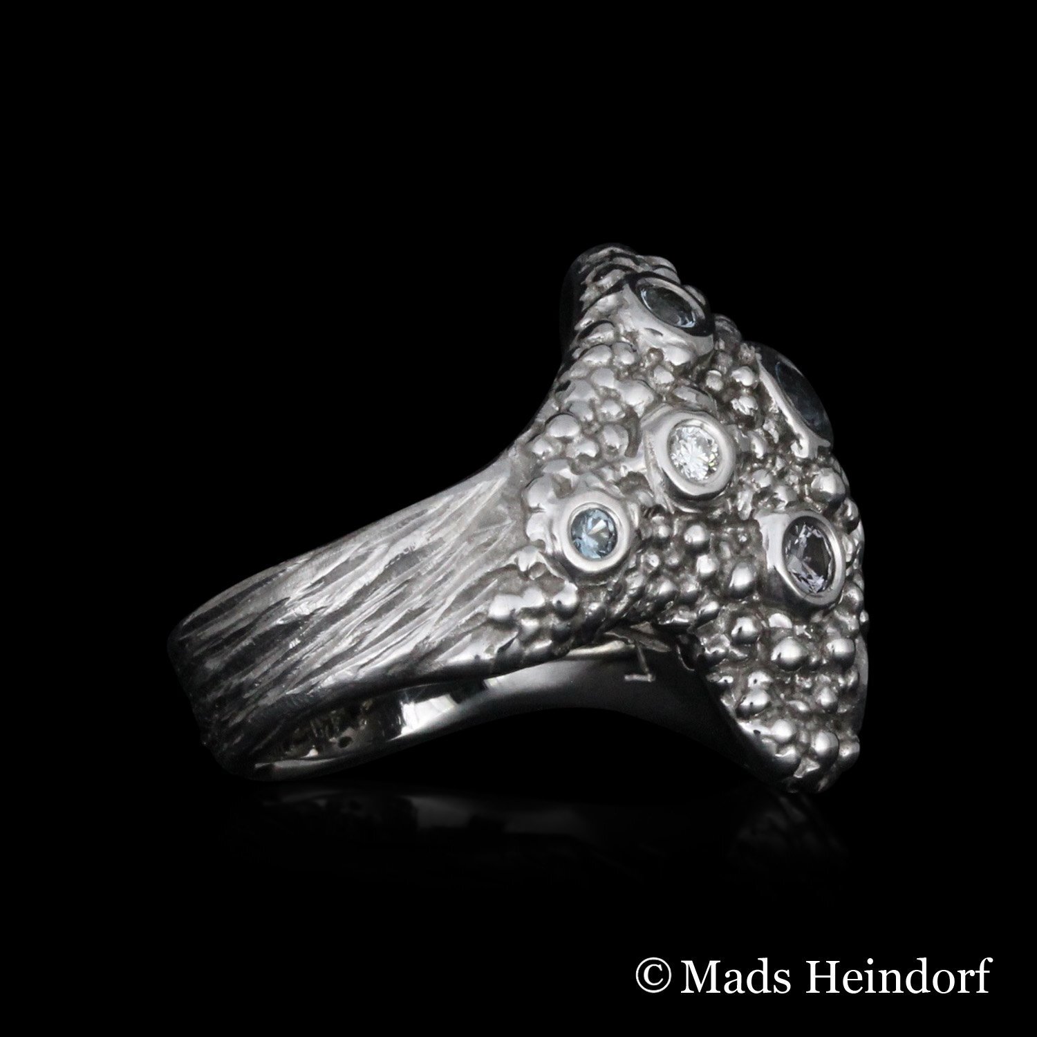 Håndlavet fingerring af 18K hvidguld med 7 blålige spineller på i alt 0,45 carat og 5 brillantslebne diamanter på i alt 0,145 carat fra kollektionen Myriader af Guldsmed Heindorf.