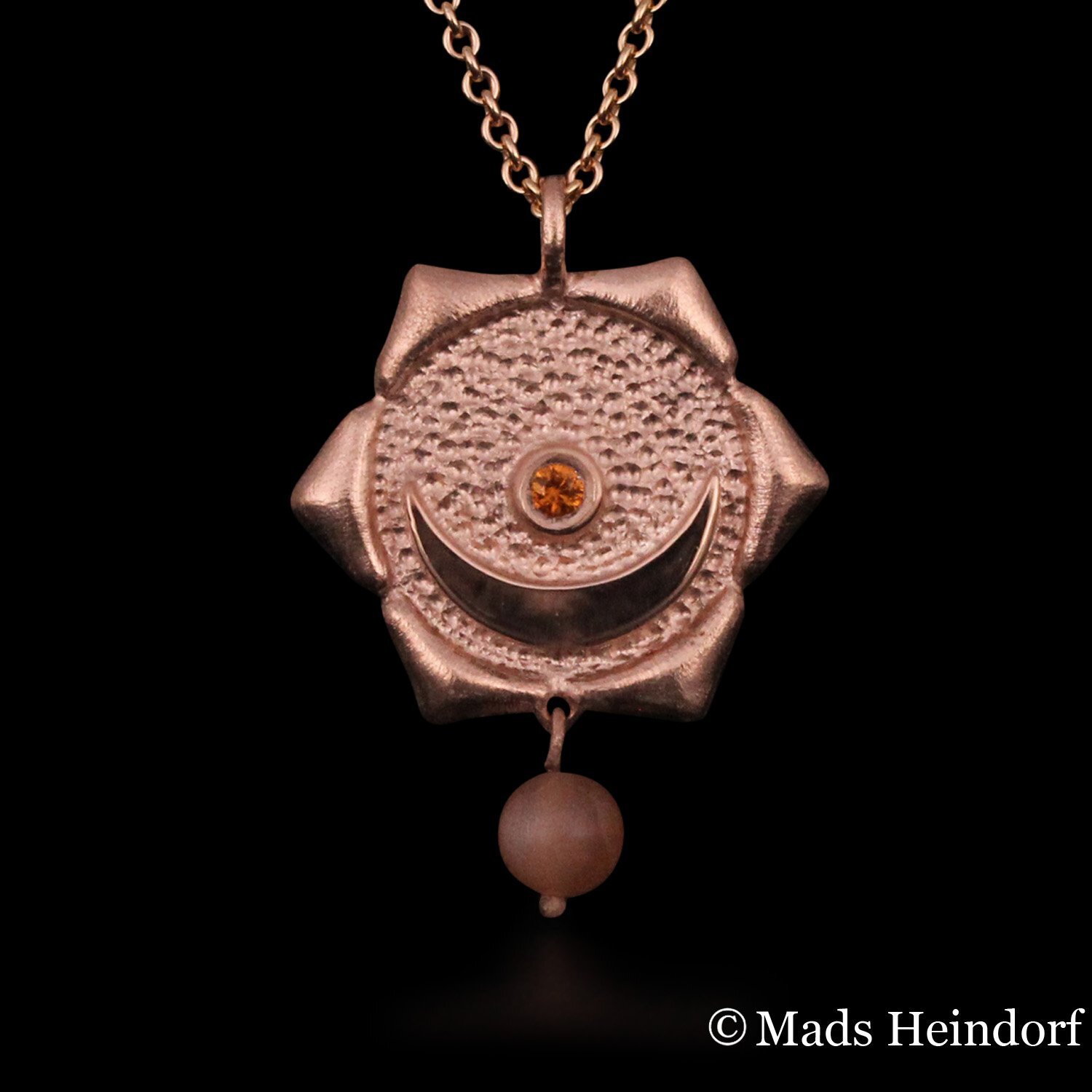 Harachakra er et håndlavet halssmykke af sterling sølv, forgyldt rosa, med 2 facetslebne orange safirer og 1 brun stenperle af solsten fra kollektionen Chakra af Guldsmed Heindorf.