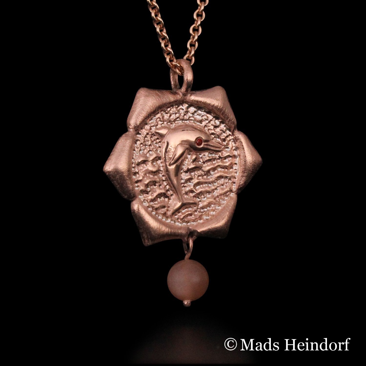 Harachakra er et håndlavet halssmykke af sterling sølv, forgyldt rosa, med 2 facetslebne orange safirer og 1 brun stenperle af solsten fra kollektionen Chakra af Guldsmed Heindorf.