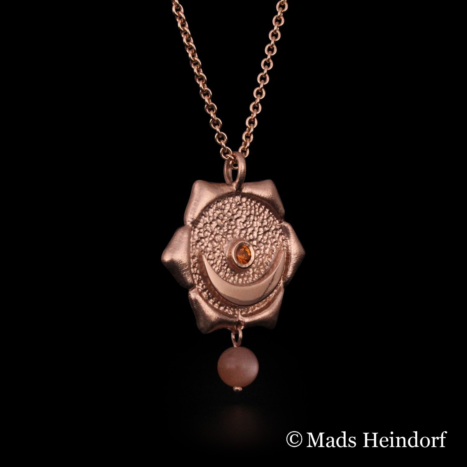 Harachakra er et håndlavet halssmykke af sterling sølv, forgyldt rosa, med 2 facetslebne orange safirer og 1 brun stenperle af solsten fra kollektionen Chakra af Guldsmed Heindorf.