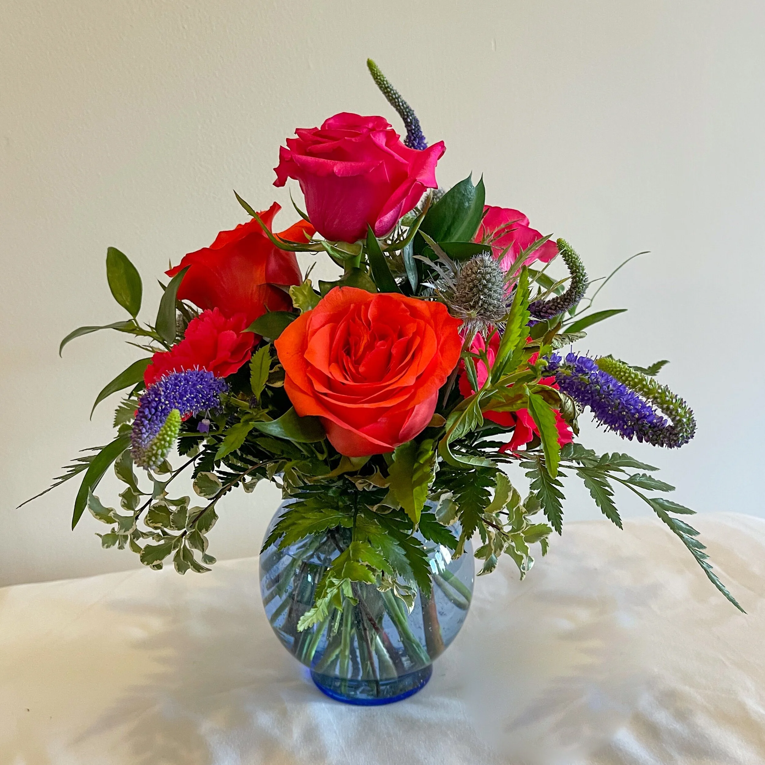 Red roses and assorted flowers and greenery in a blue bubble vase