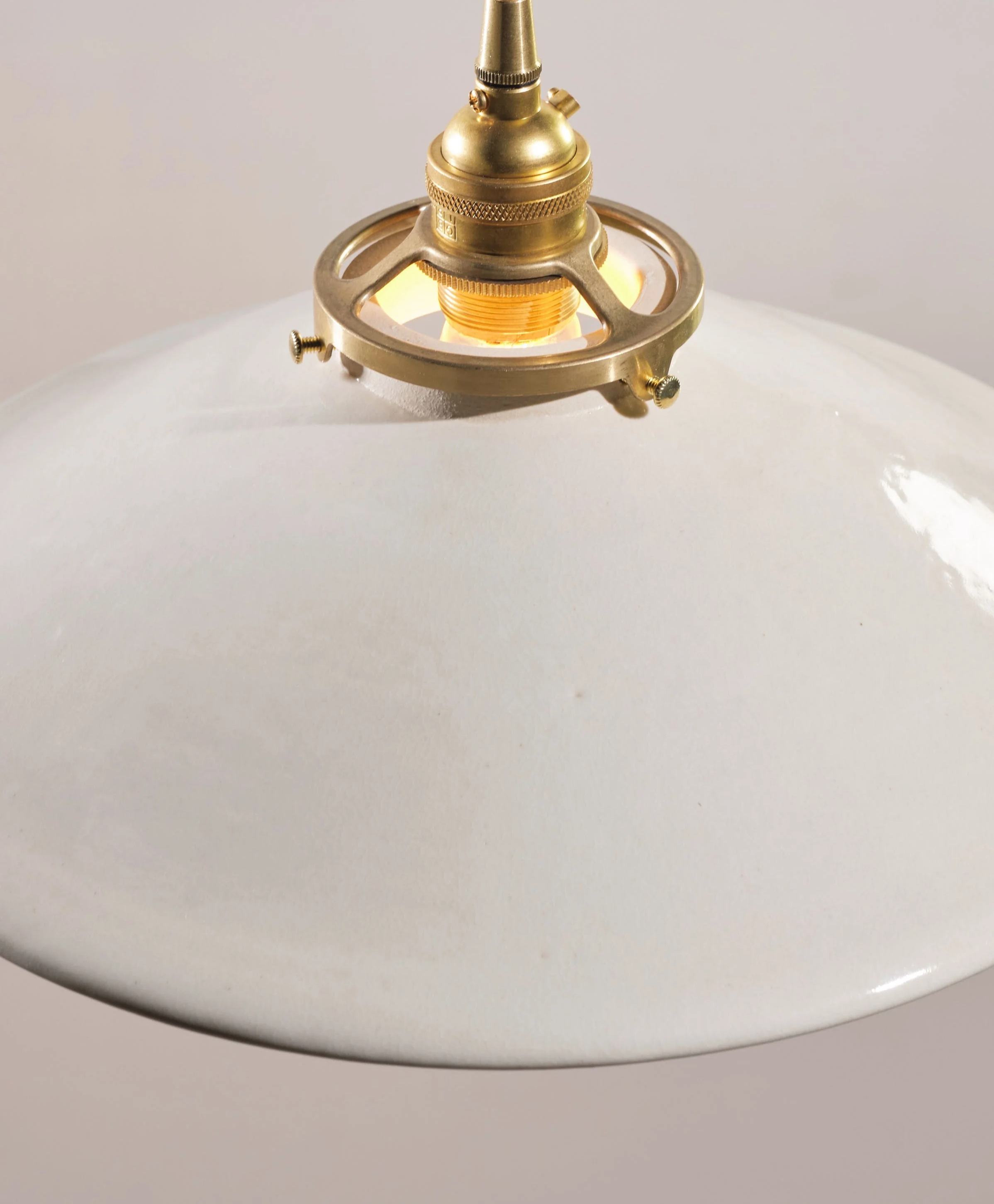 Close-up of a brass hanging fixture on white ceramic, handmade pendant shade.