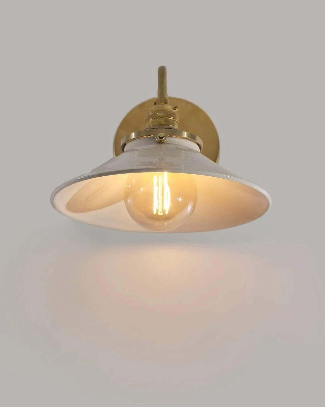 Handmade ceramic sconce with a transparent bulb and brass hardware mounted on a white wall.