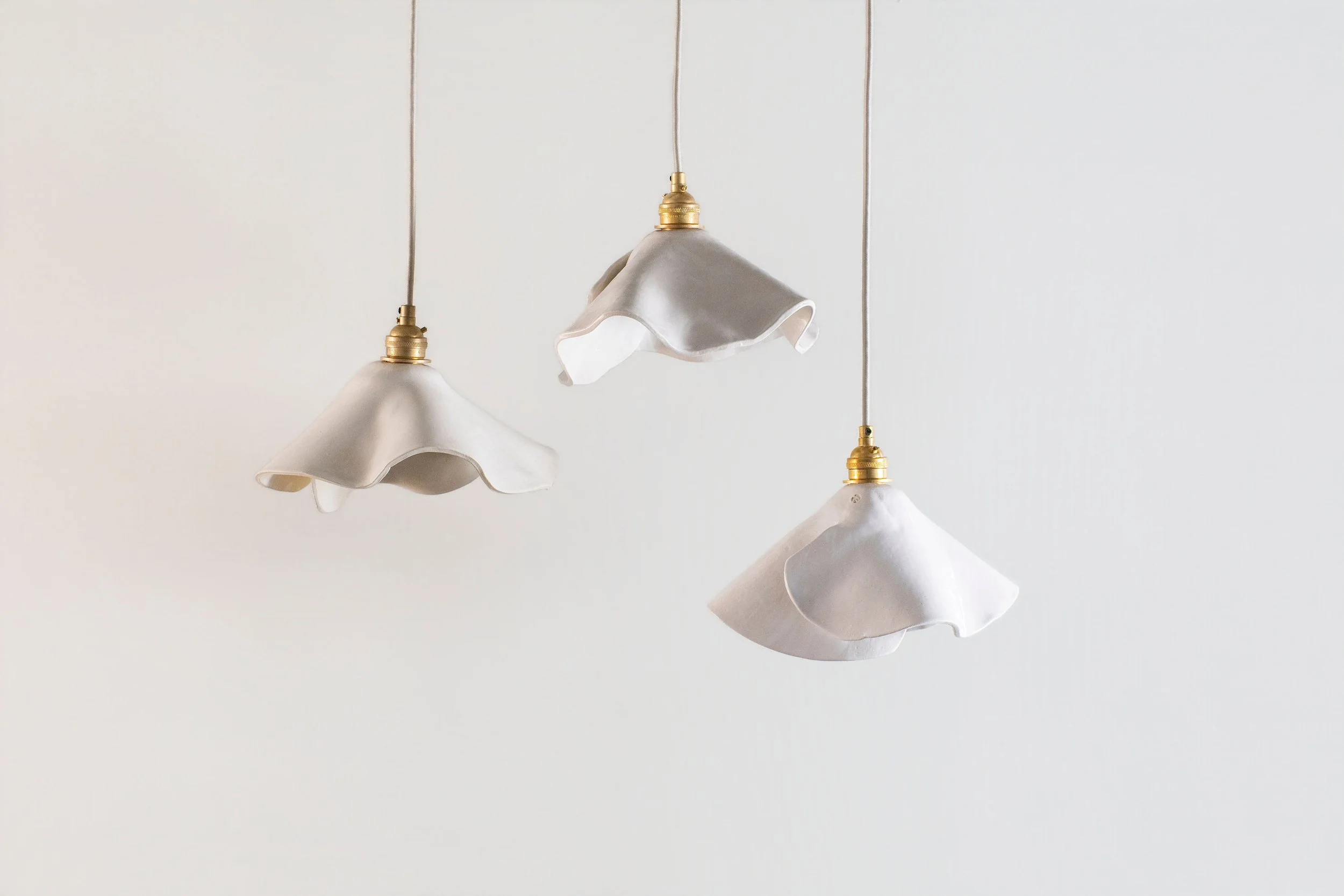Three hanging ceramic pendant lights with organic shapes, brass hardware and antique cording.