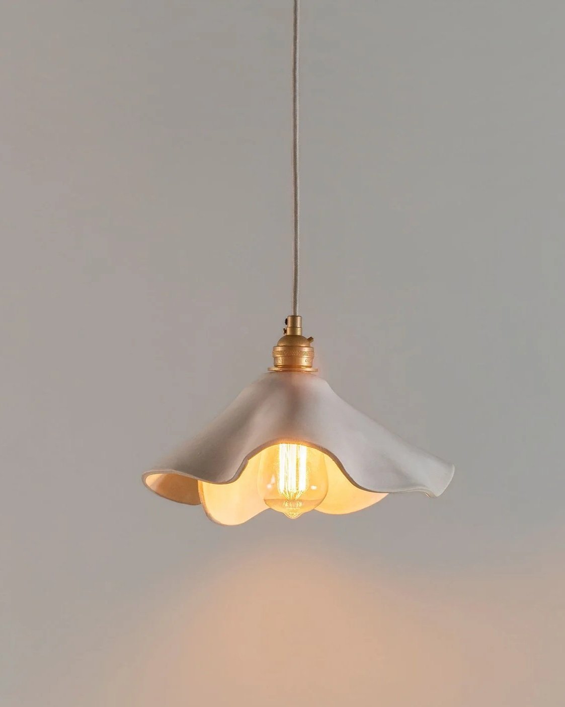 Modern hanging pendant light with a draped, art nouveau shade and vintage-style filament bulb, suspended from the ceiling from a cloth cord.