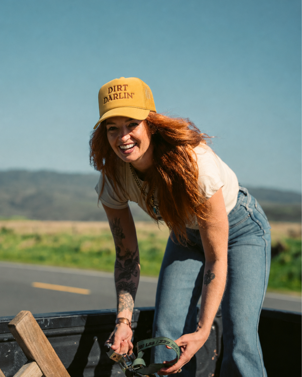 Jessyjo Darling wearing a gold Dirt Darlin trucker hat outdoors in the mountains.