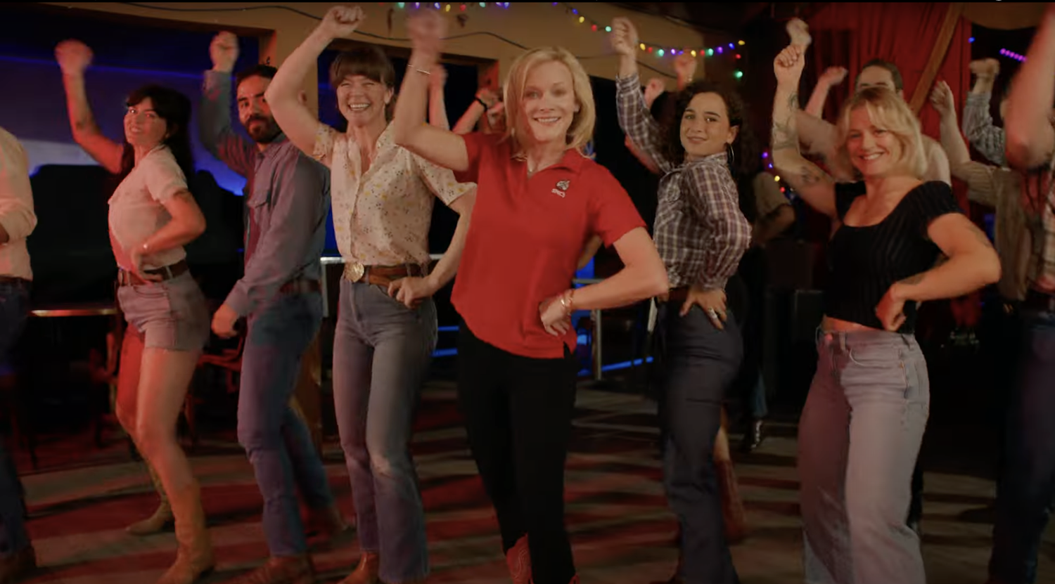 A room of dancers line dancing in unison behind a woman in a red polo shirt in the Spec's commercial