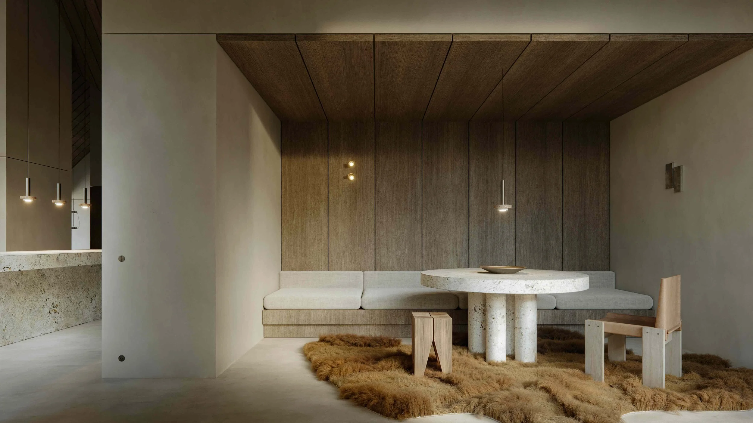 Modern dining nook with a round stone table, beige built-in sofa, wooden chair, and faux fur rug beneath the table, with wood-paneled wall background and minimal pendant lighting.