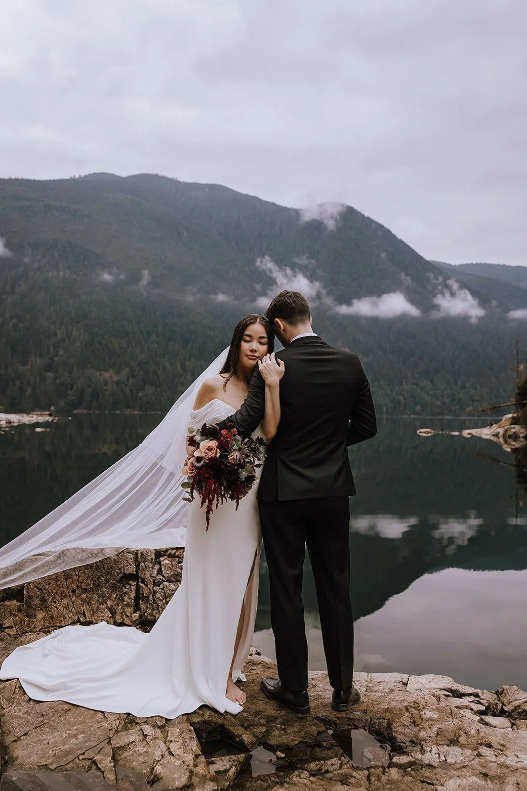 A bride and groom embrace under the mountains of Golden Ears Provincial Park